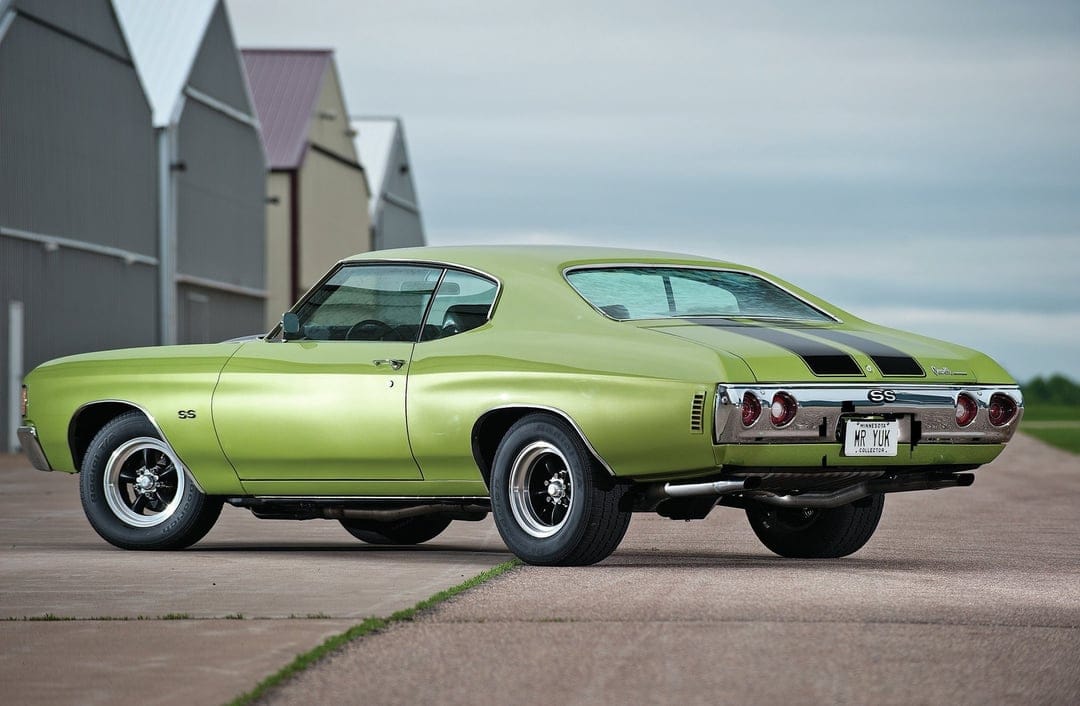 Lime green Chevrolet Chevelle SS muscle car with black stripes parked on asphalt near industrial buildings.