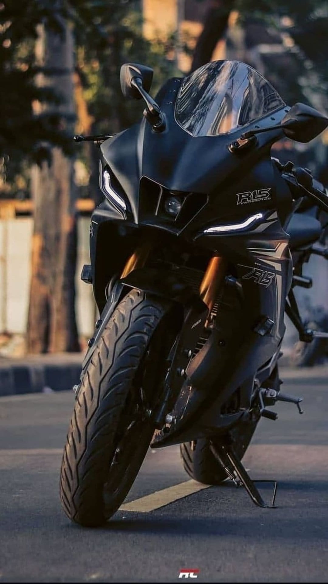 Matte black Yamaha R15 motorcycle featuring LED headlights and front tire with blurred trees in the background.