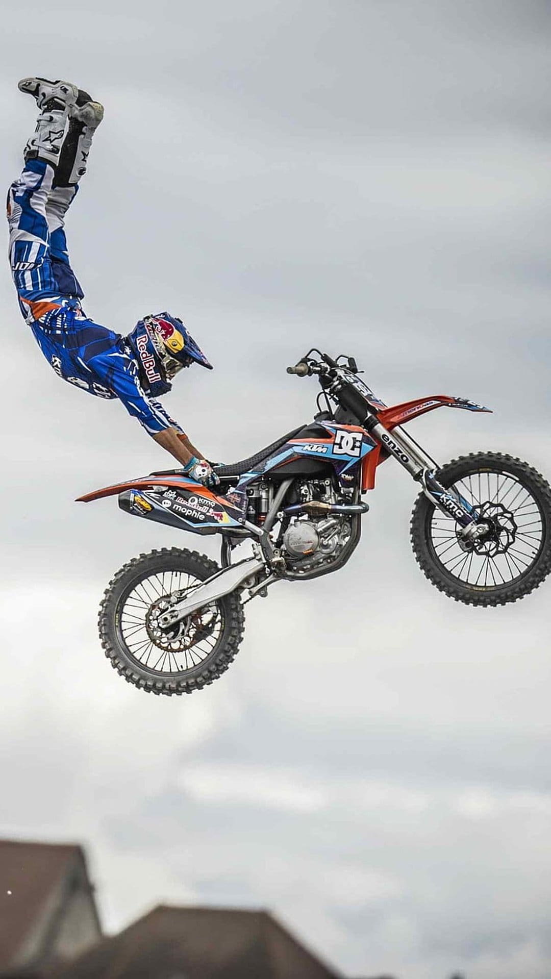 Motocross rider performs a mid-air grab on a KTM dirt bike against a cloudy sky in this vertical action photo.