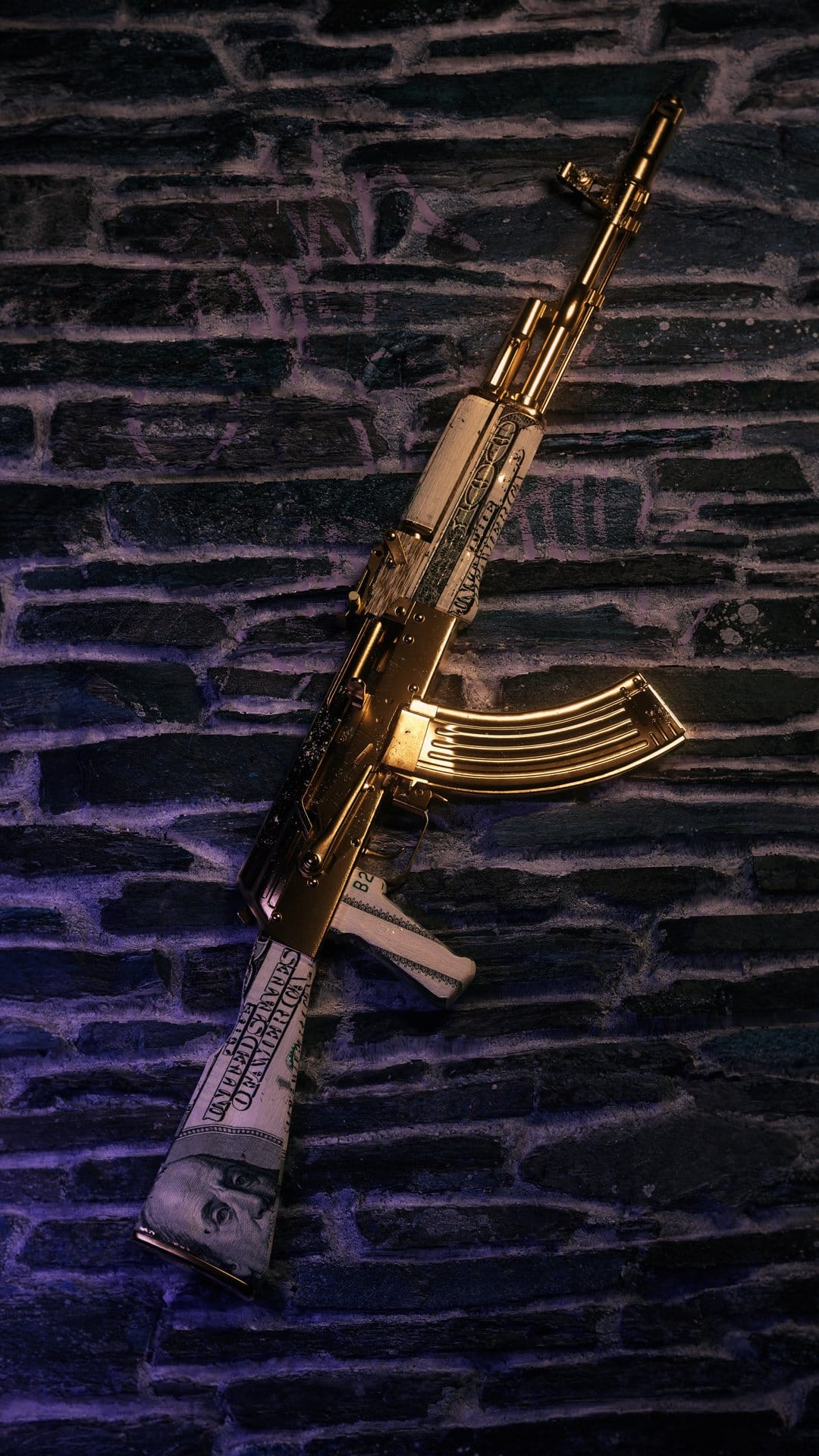 Gold AK-47 rifle covered in US dollar bills rests against a dark brick wall with faint purple lighting.