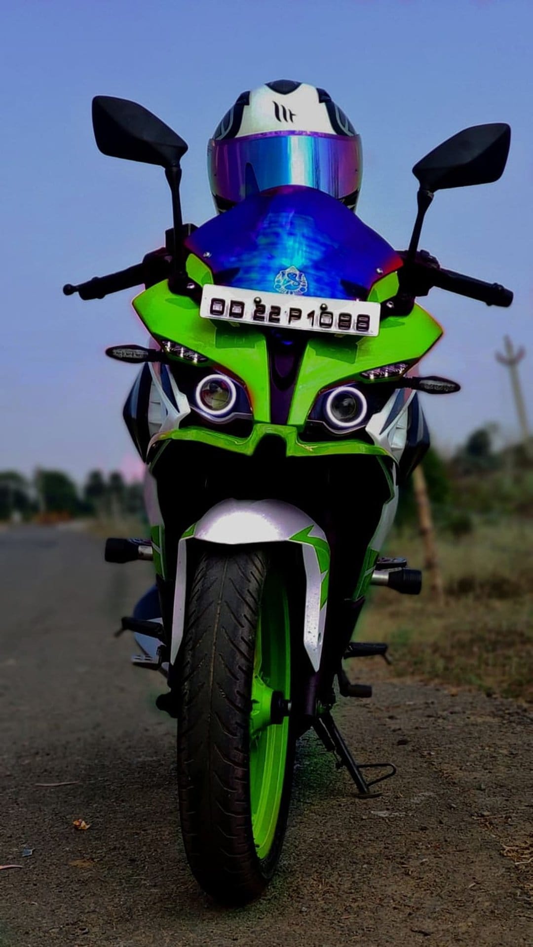 Green sport motorcycle with glowing halo headlights and a helmet featuring a reflective blue visor.
