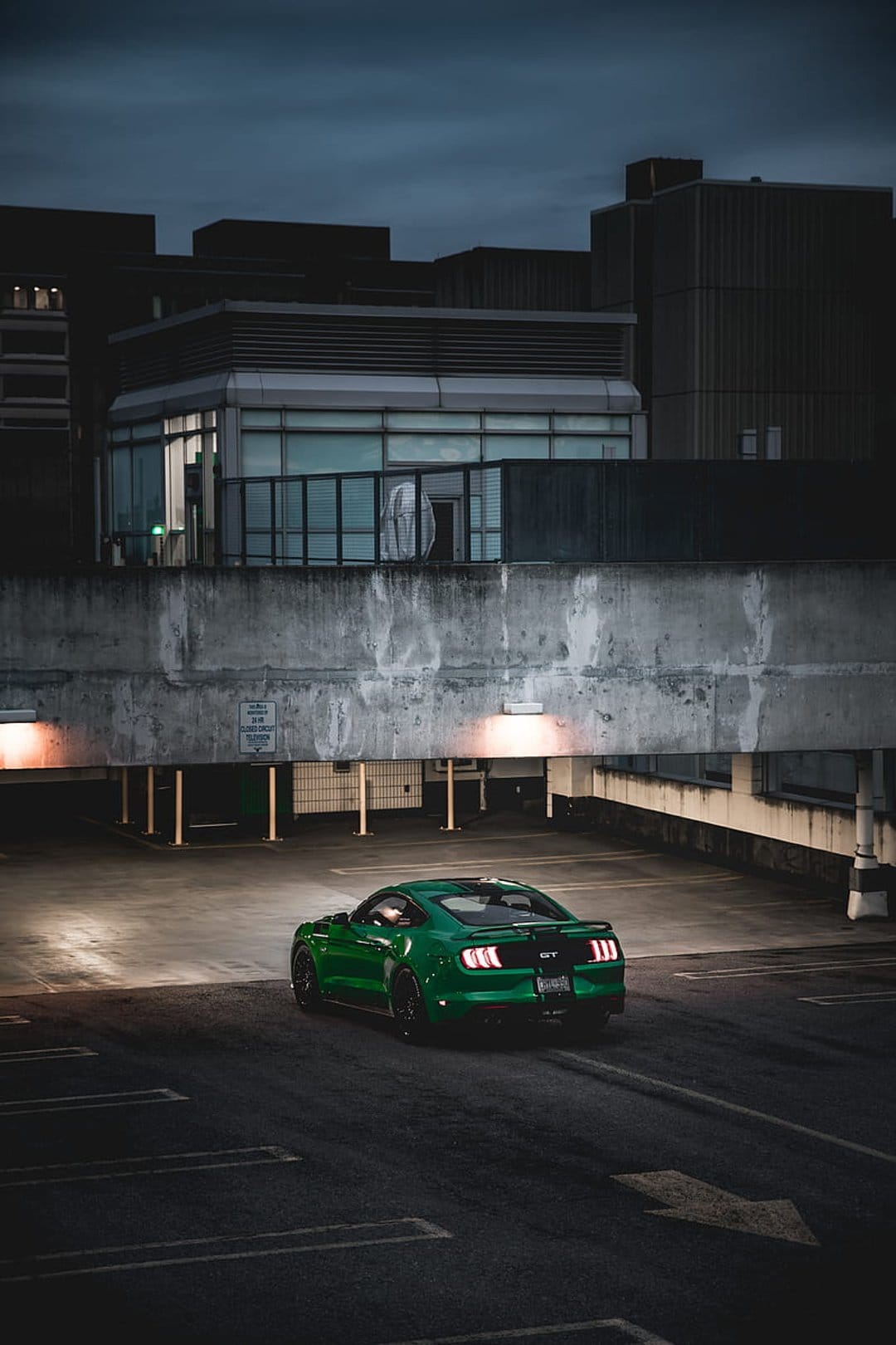 Green Mustang GT sports car parked in a shadowed concrete garage with artificial lights reflecting on its paint.