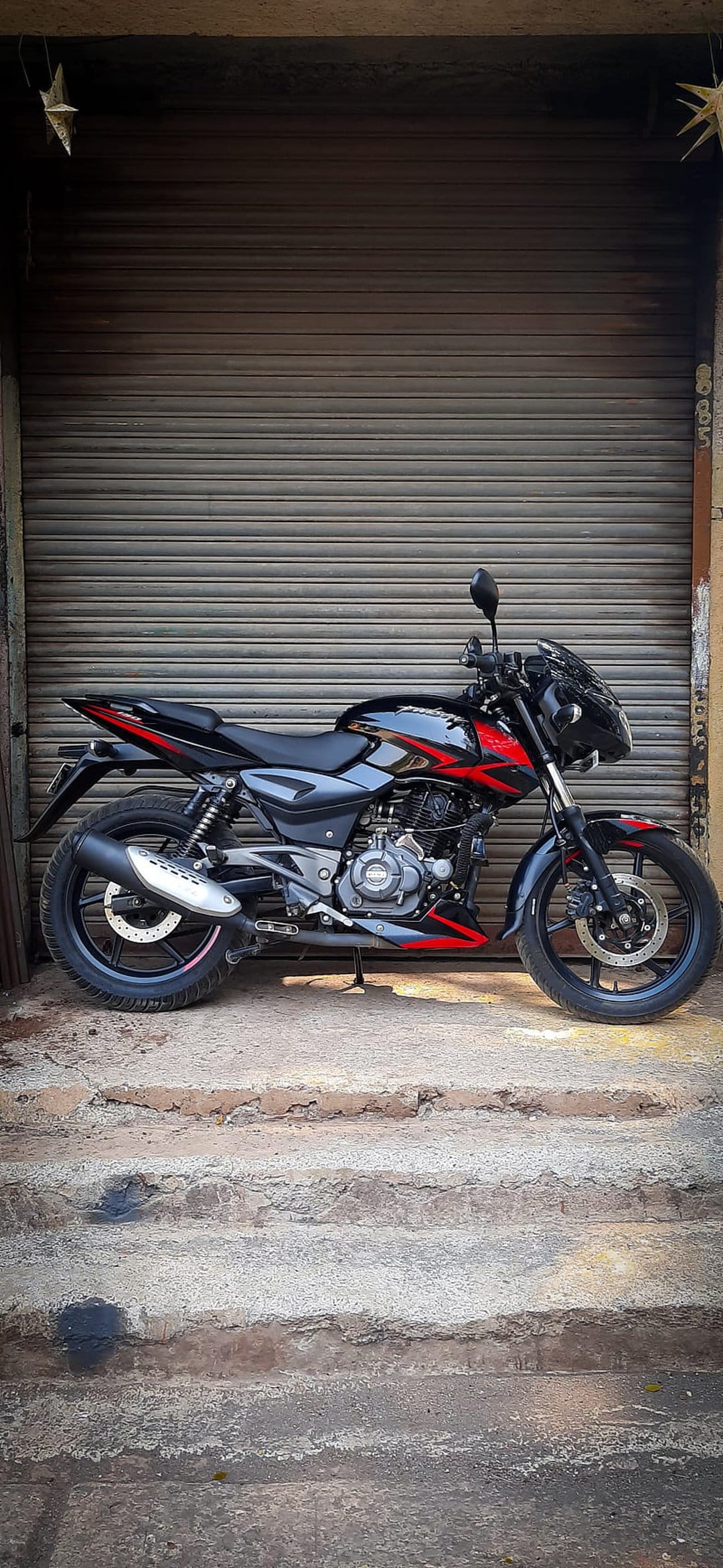 Black sportbike with red accents parked on concrete steps in front of a corrugated metal garage door in an alley.