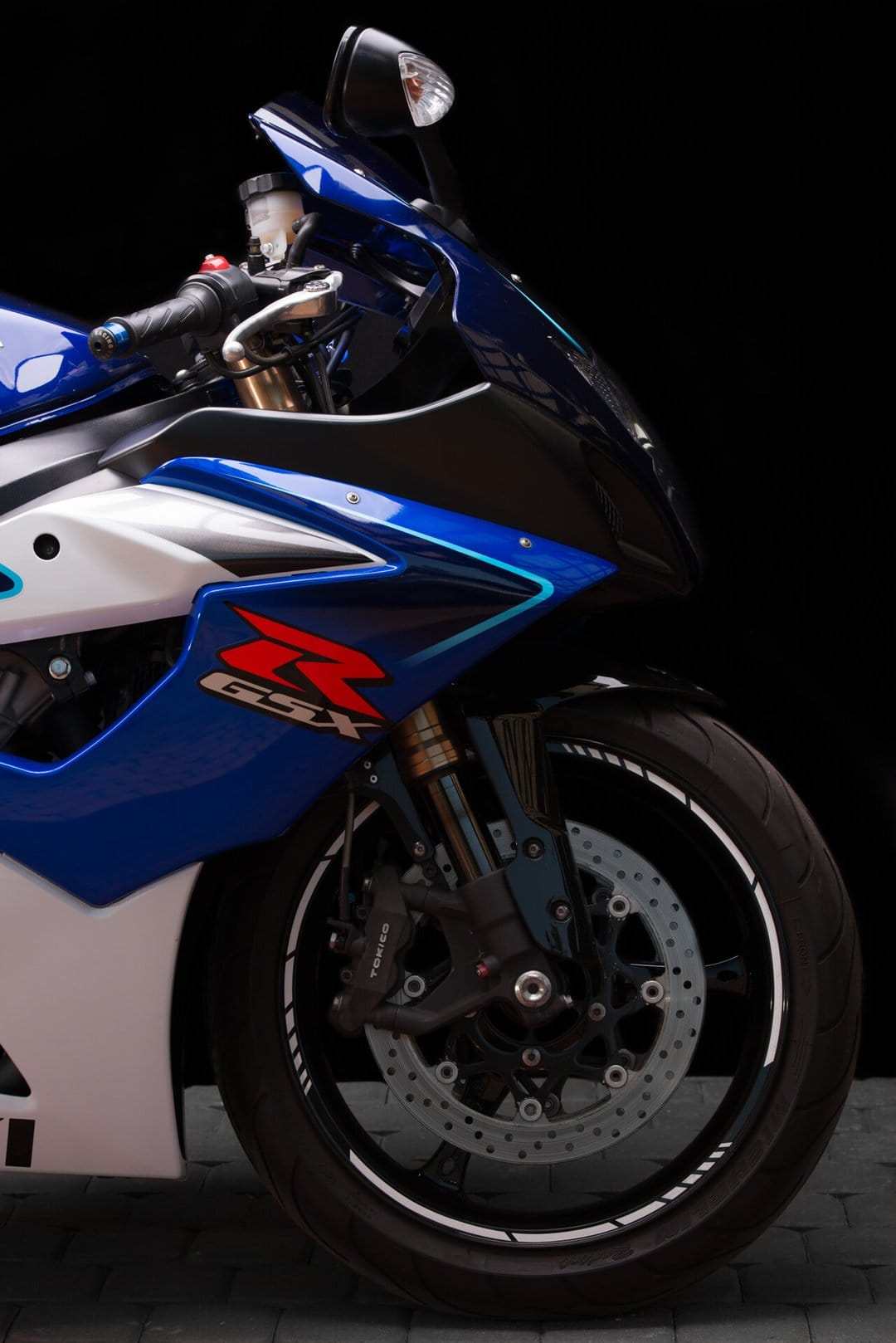 Detailed front view of a blue and white Suzuki GSX-R motorcycle with Tokico brakes on a black background.