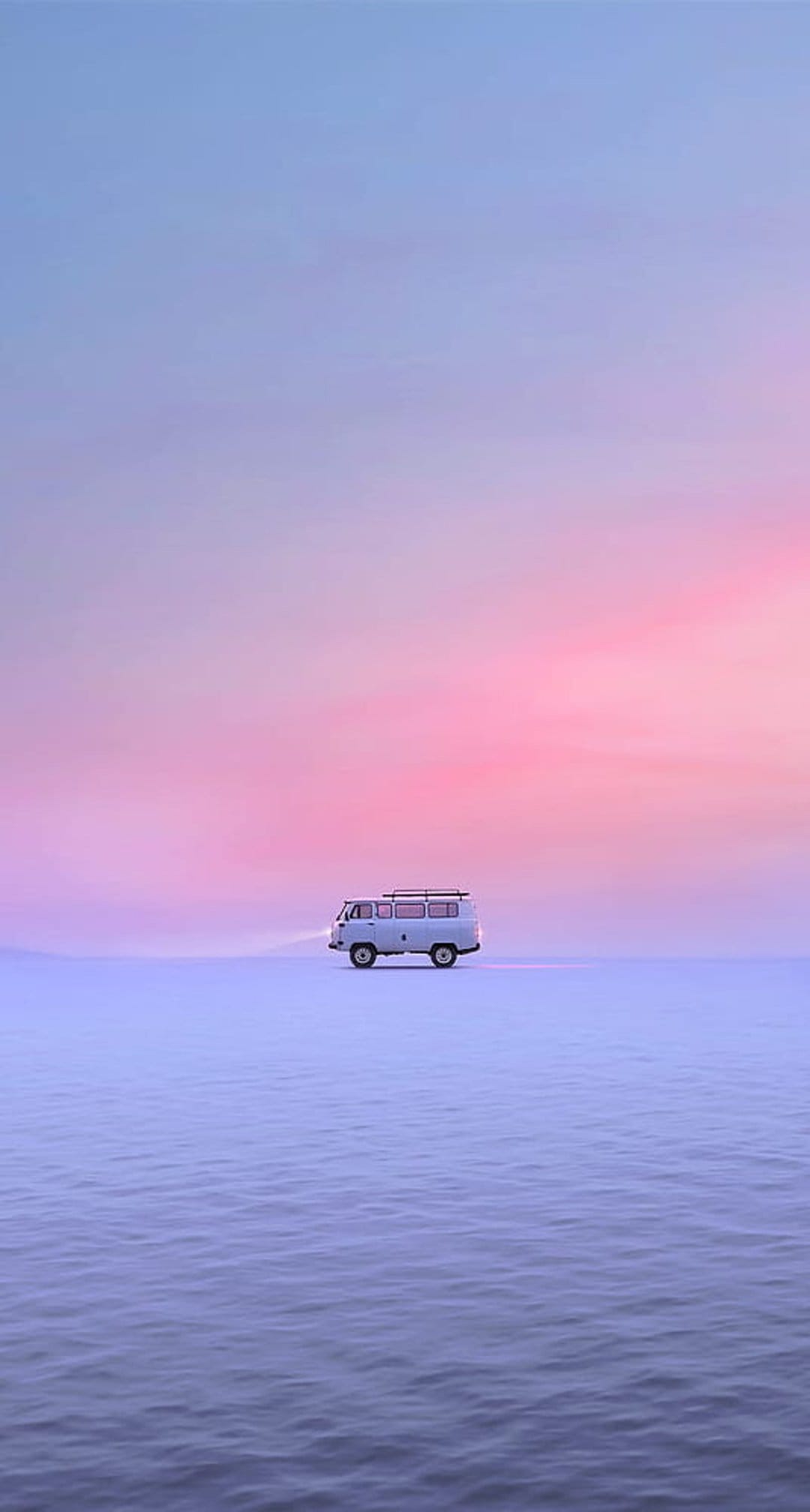 White van with glowing headlights driving across a reflective water surface under a pink and purple sunset sky.