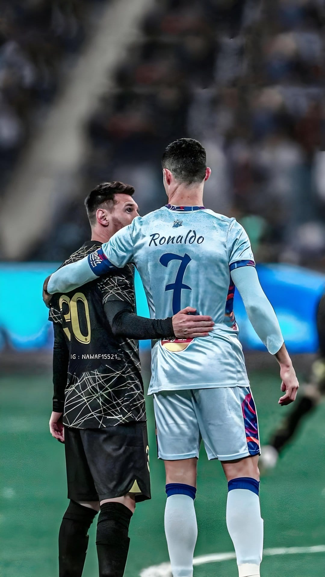 Lionel Messi and Cristiano Ronaldo hug on a soccer field under bright stadium lights during an evening match.
