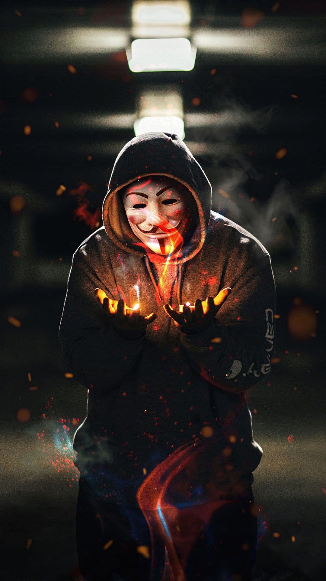 Masked person in a black hoodie holding a glowing ball of fire and orange sparks against a dark background.
