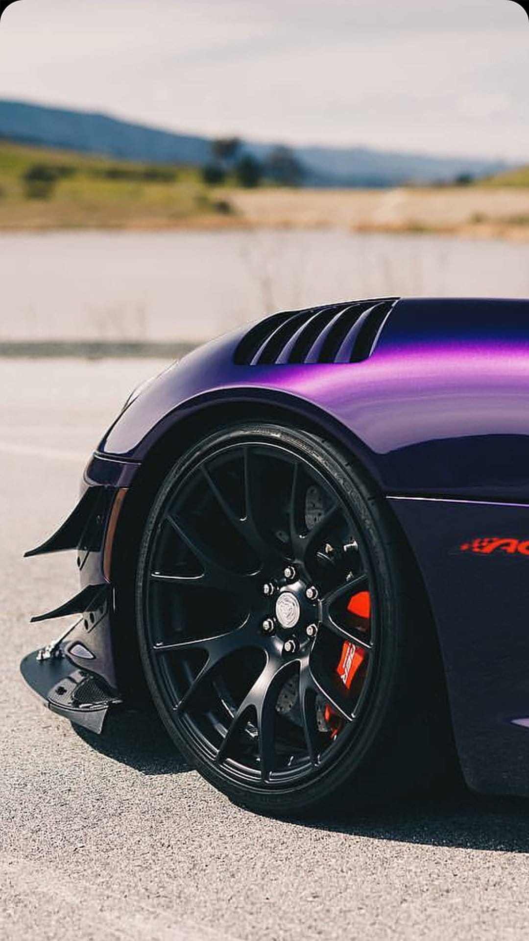 Purple Dodge Viper SRT 10 front fender and black multi-spoke wheel with red brake calipers on a scenic road.