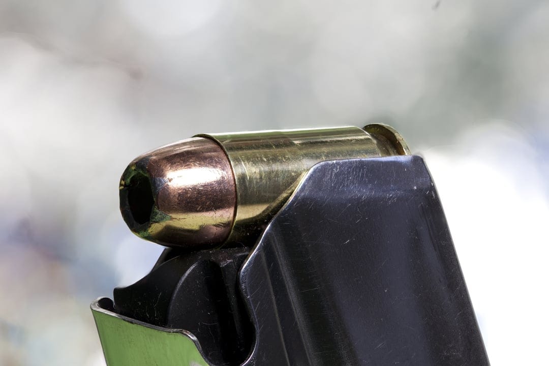 Brass 9mm bullet seated in a black metal magazine with a shallow depth of field and blurred background.