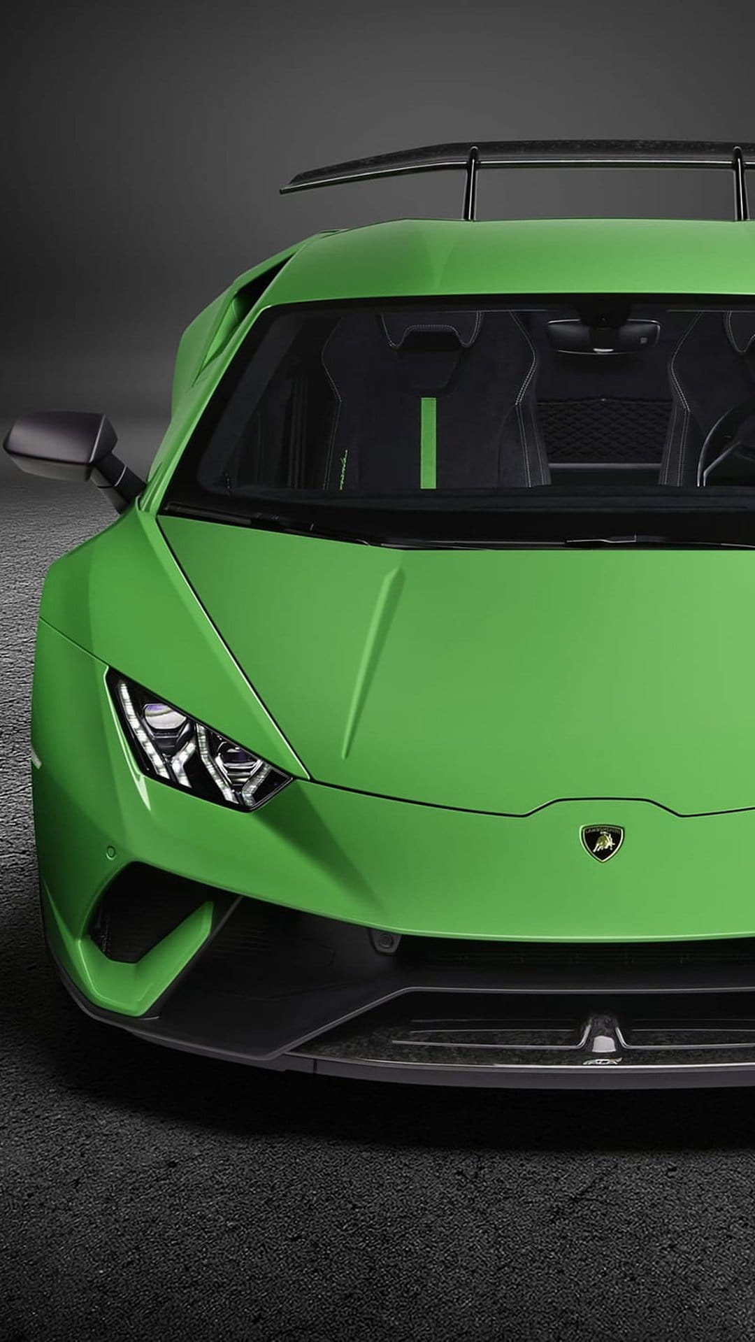 Lime green Lamborghini Huracan STO showing aggressive front air intakes and headlights on a textured road.