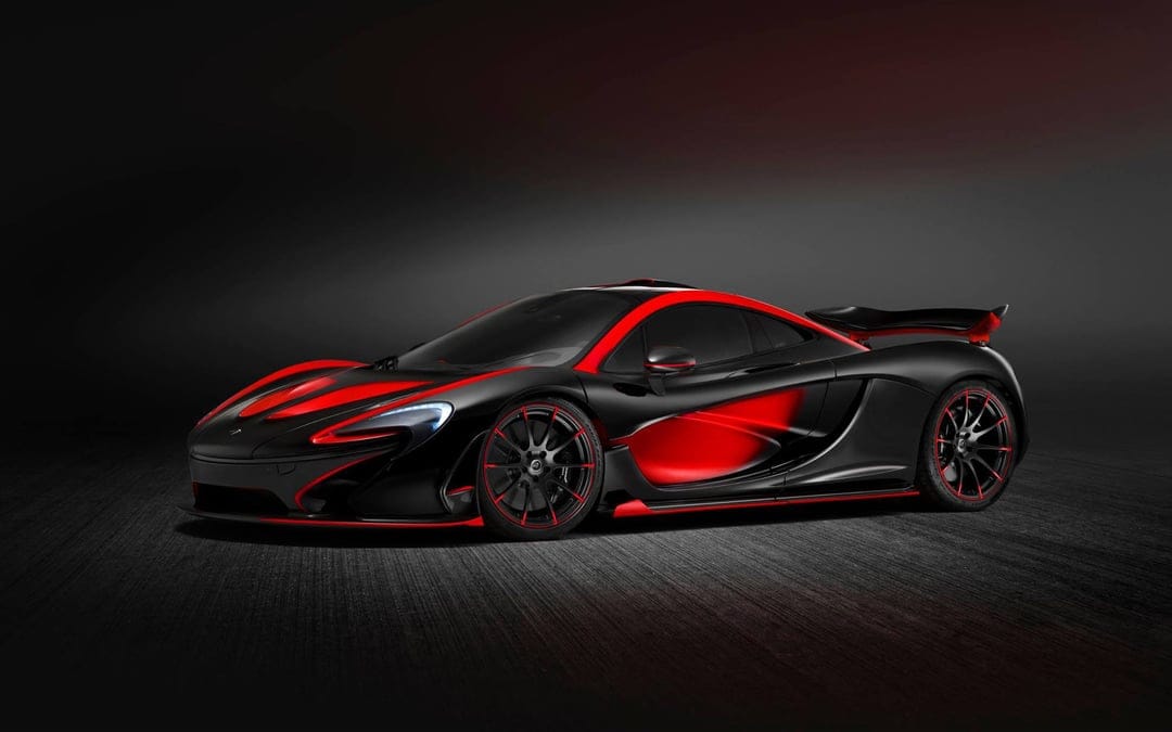 Side profile of a black McLaren P1 supercar with vibrant red accents on wheels and body in a dark studio.