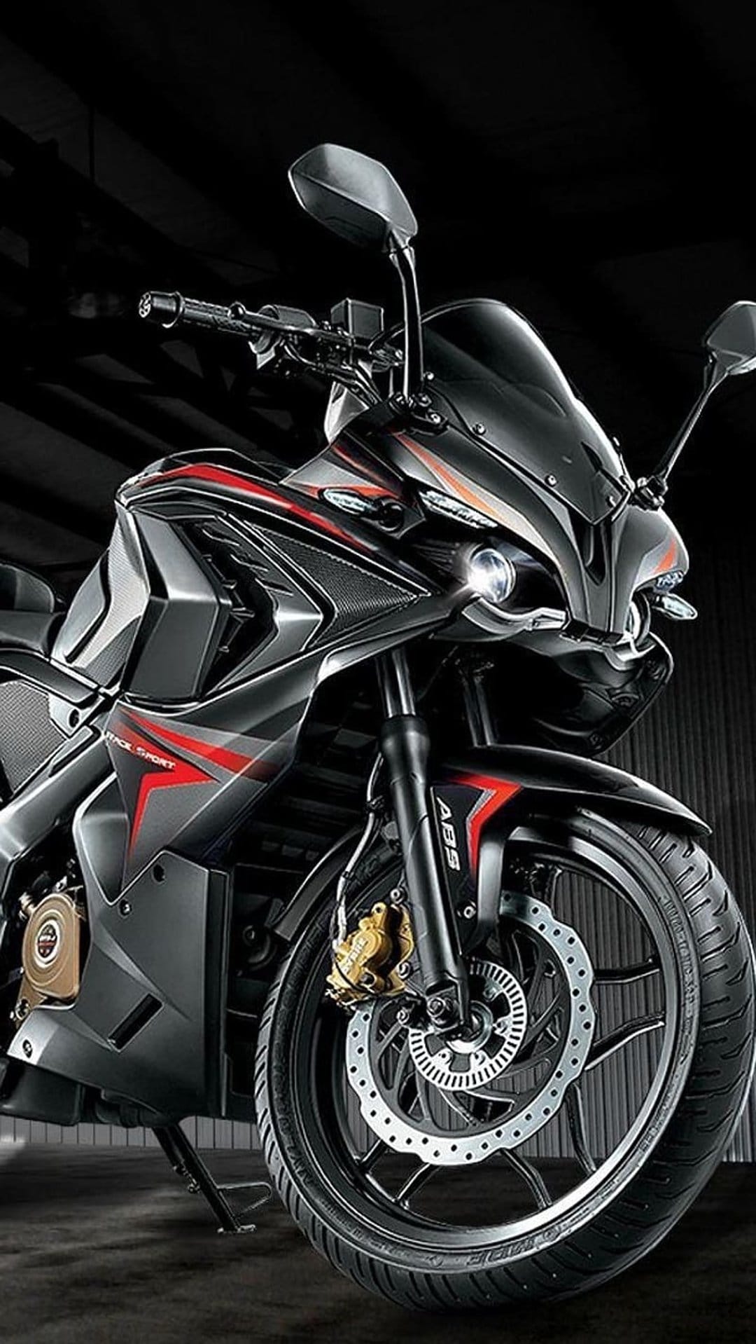 Black sportbike with red stripes and glowing headlights sits against a dark backdrop in a close-up profile view.