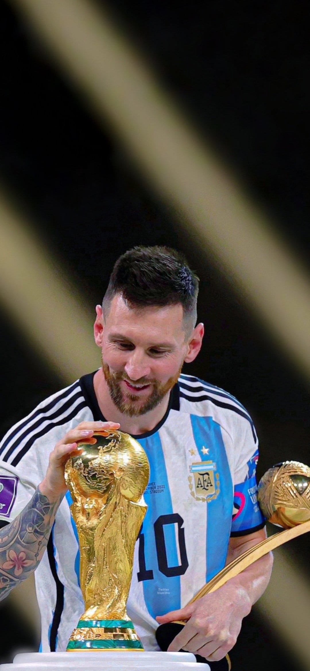 Lionel Messi smiles and holds the golden FIFA World Cup trophy while wearing an Argentina national team jersey.