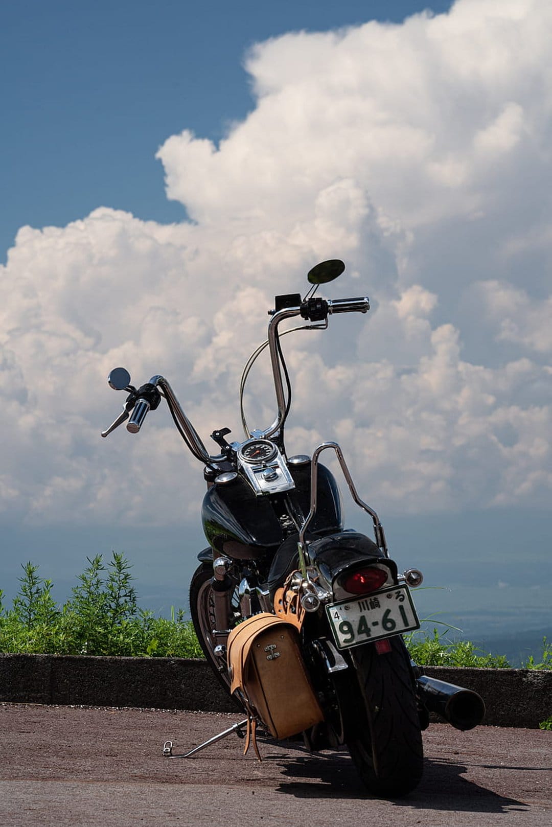 Black Harley-Davidson motorcycle with tan saddlebags parked at a roadside overlook under a bright cloudy sky.