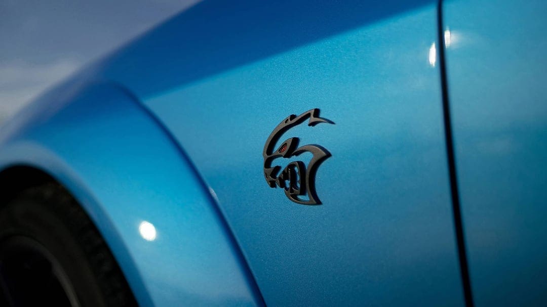 Black SRT Hellcat logo on metallic blue car paint with shallow depth of field and soft outdoor lighting.