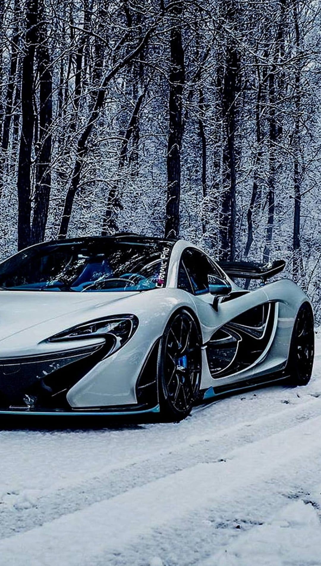 White McLaren P1 supercar parked on a snow-covered forest road during winter with frost-laden evergreen trees.