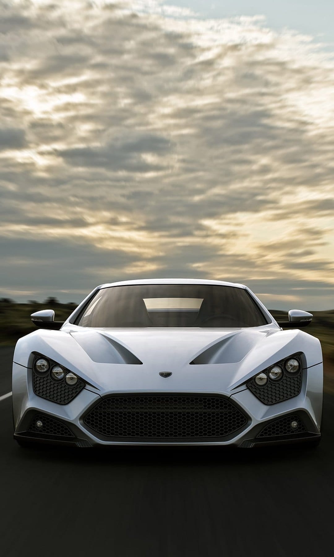 Zenvo ST1 white hypercar drives on a road under a grey overcast sky with motion blur on the asphalt.