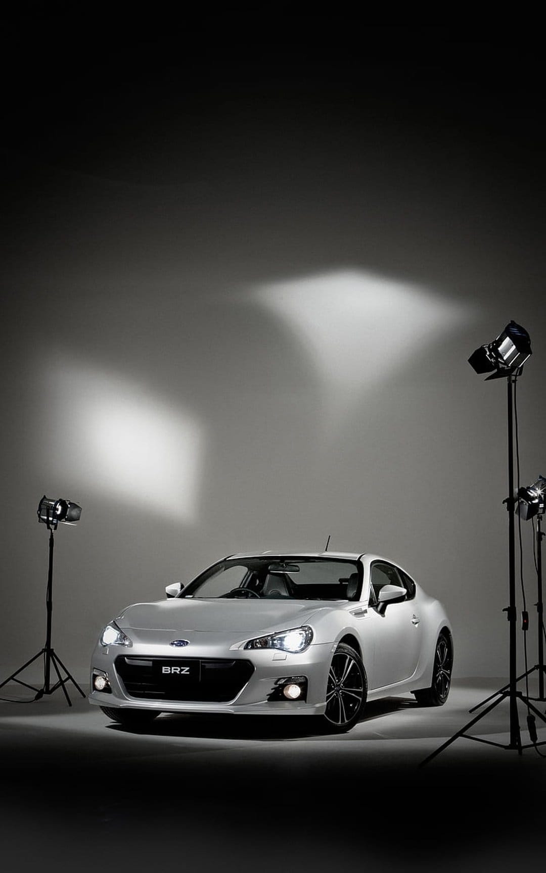 Silver Subaru BRZ sports car features dramatic studio lighting against a gray gradient background in portrait.
