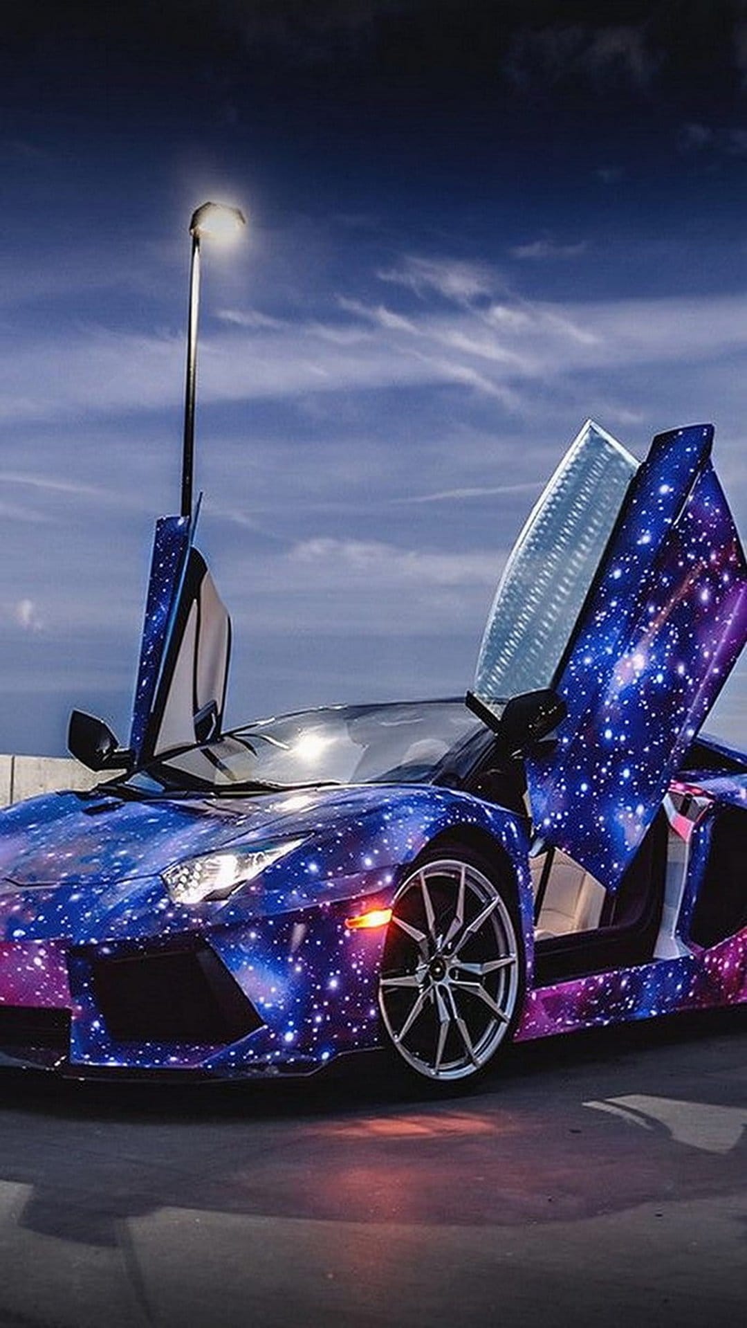 Lamborghini Aventador with a galaxy wrap and open scissor doors parked under a cloudy sky and a street lamp.
