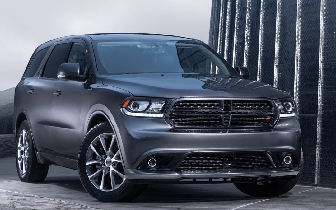 Metallic grey Dodge Durango SUV parked outdoors against a modern reflective building with bright LED headlights.
