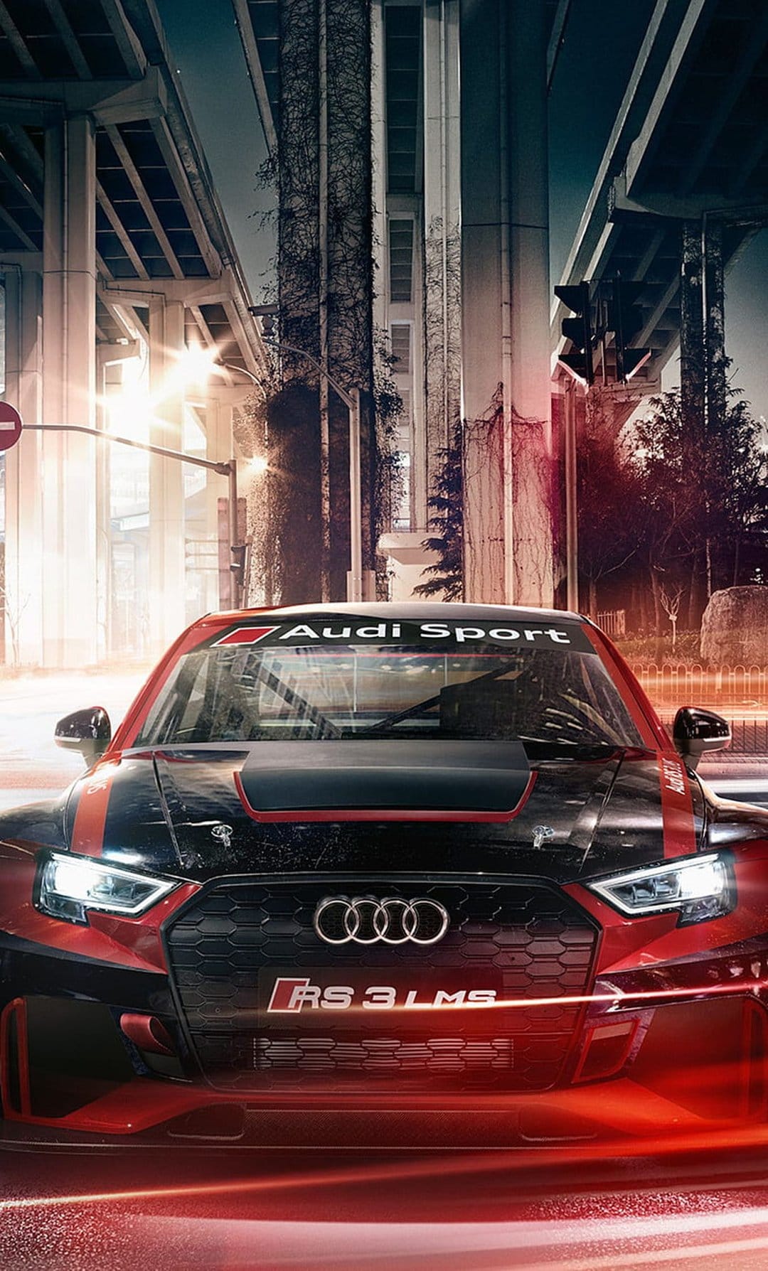 Audi RS3 LMS race car with red and black livery parked on a dark city street illuminated by golden urban lights.
