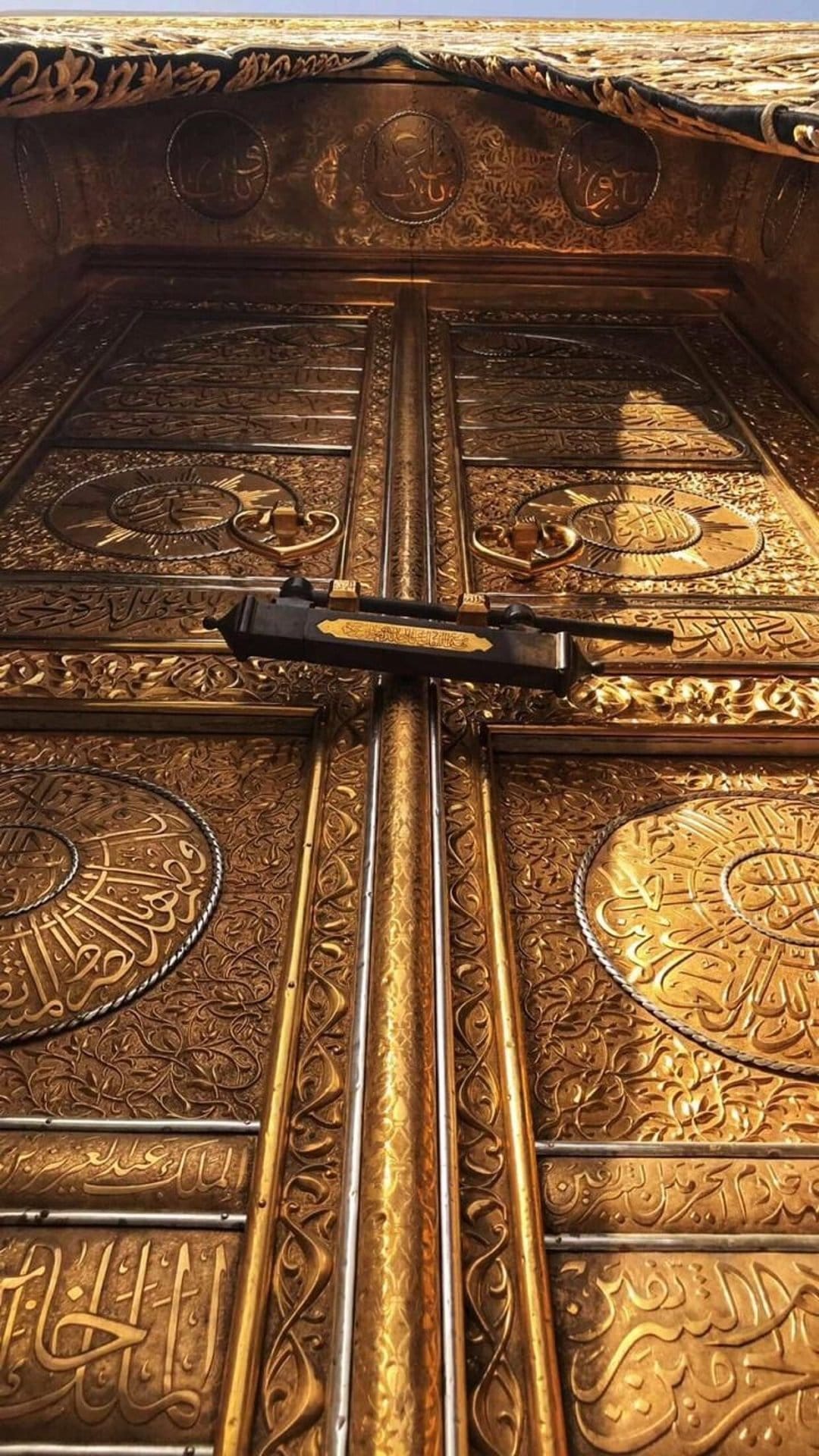 Golden Kaaba door with raised Arabic calligraphy and a black metal lock in a detailed vertical close-up.