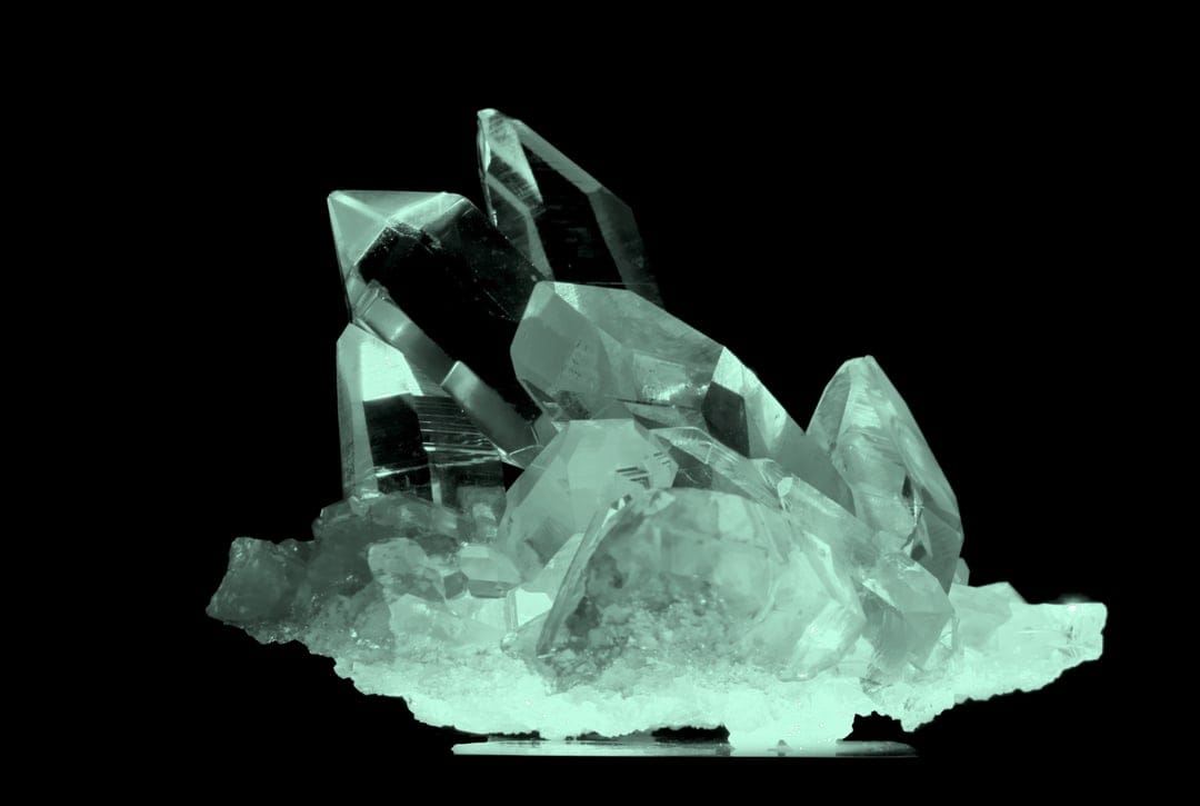 Clear quartz crystal cluster with sharp hexagonal points and transparent facets on a solid black background.