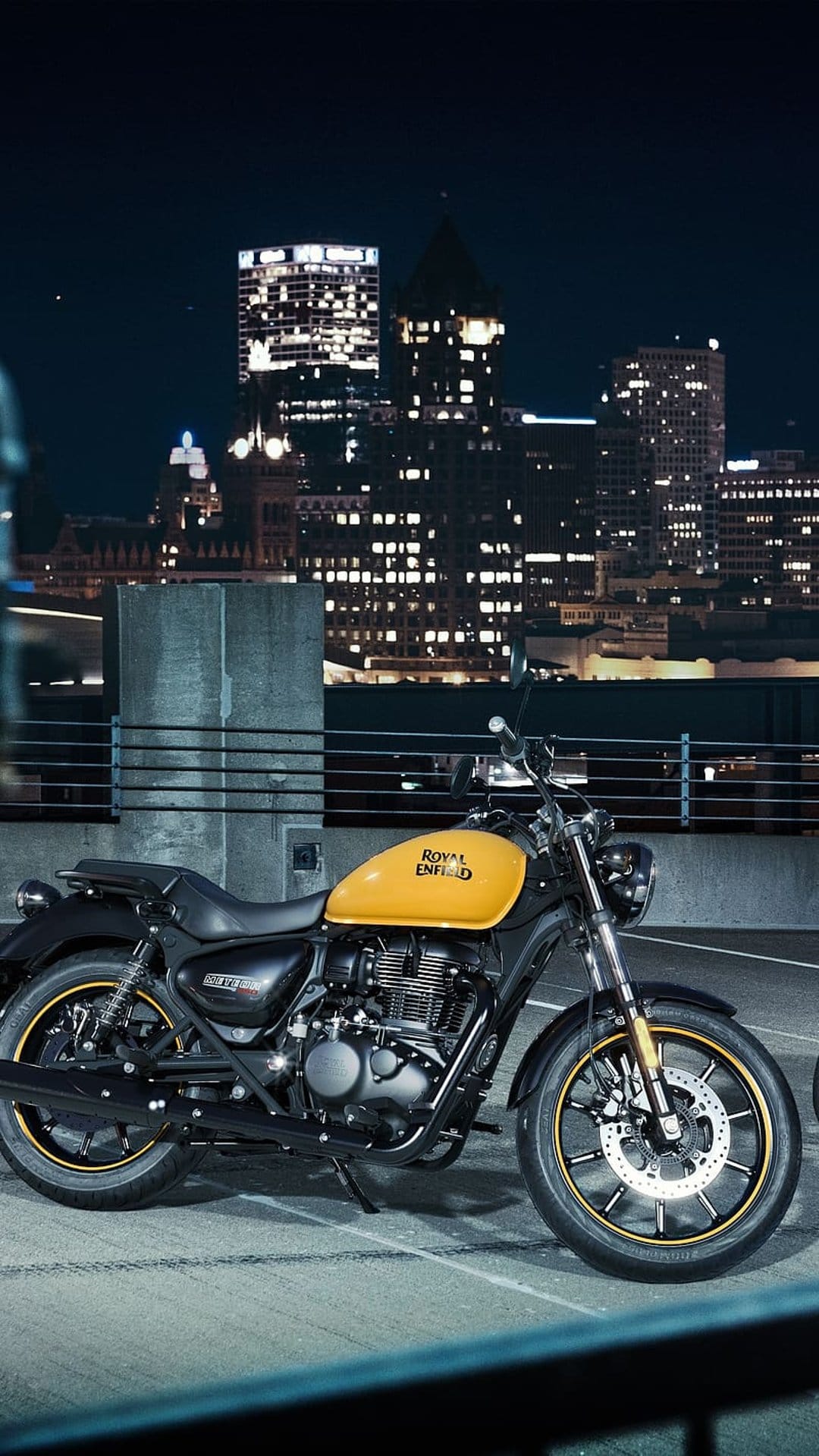 Yellow Royal Enfield motorcycle with chrome accents parked in a city at night with blurred background lights.