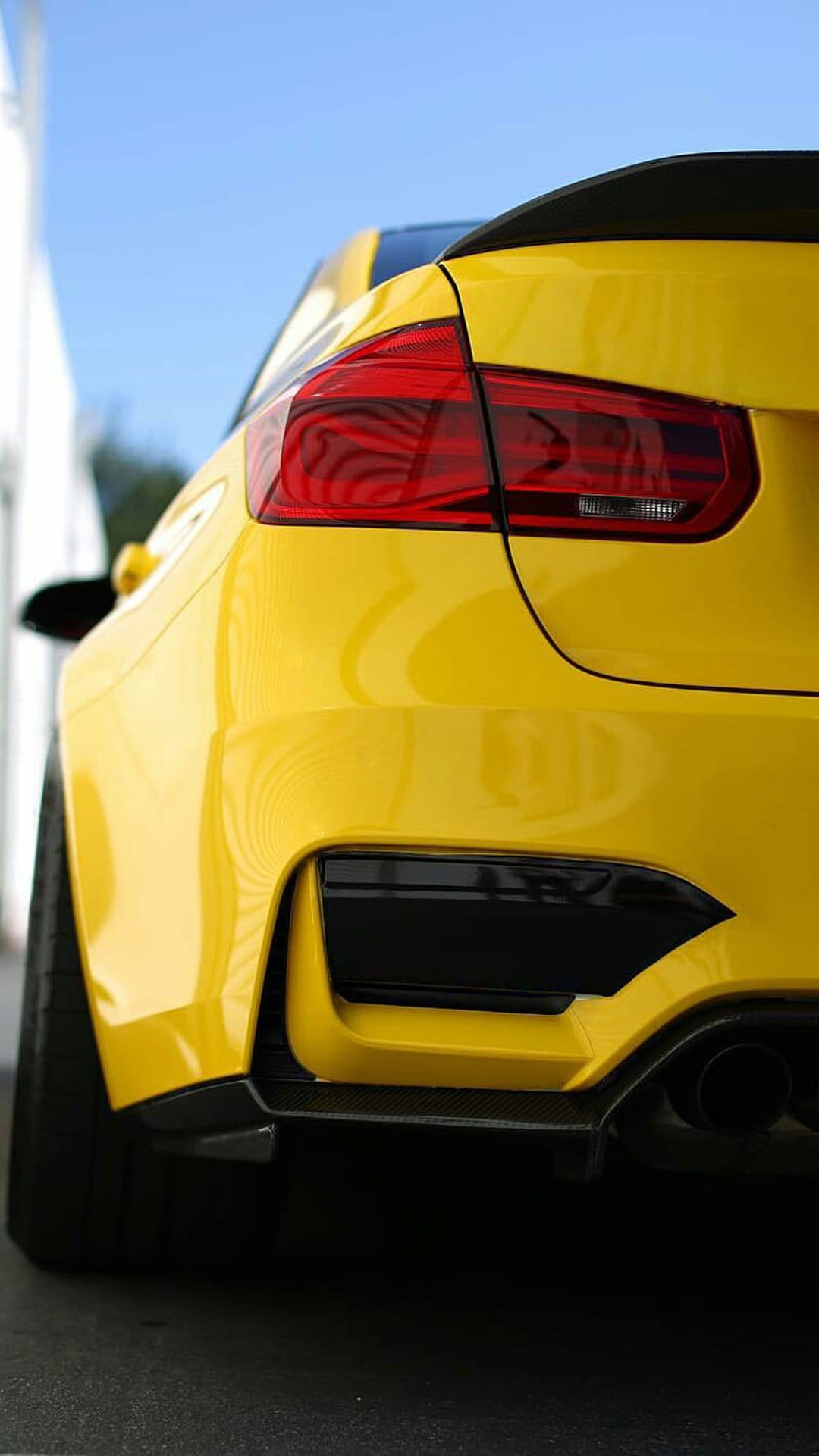 Yellow BMW M4 rear bumper showing red LED taillights, black carbon fiber diffuser, and sleek metallic paint.