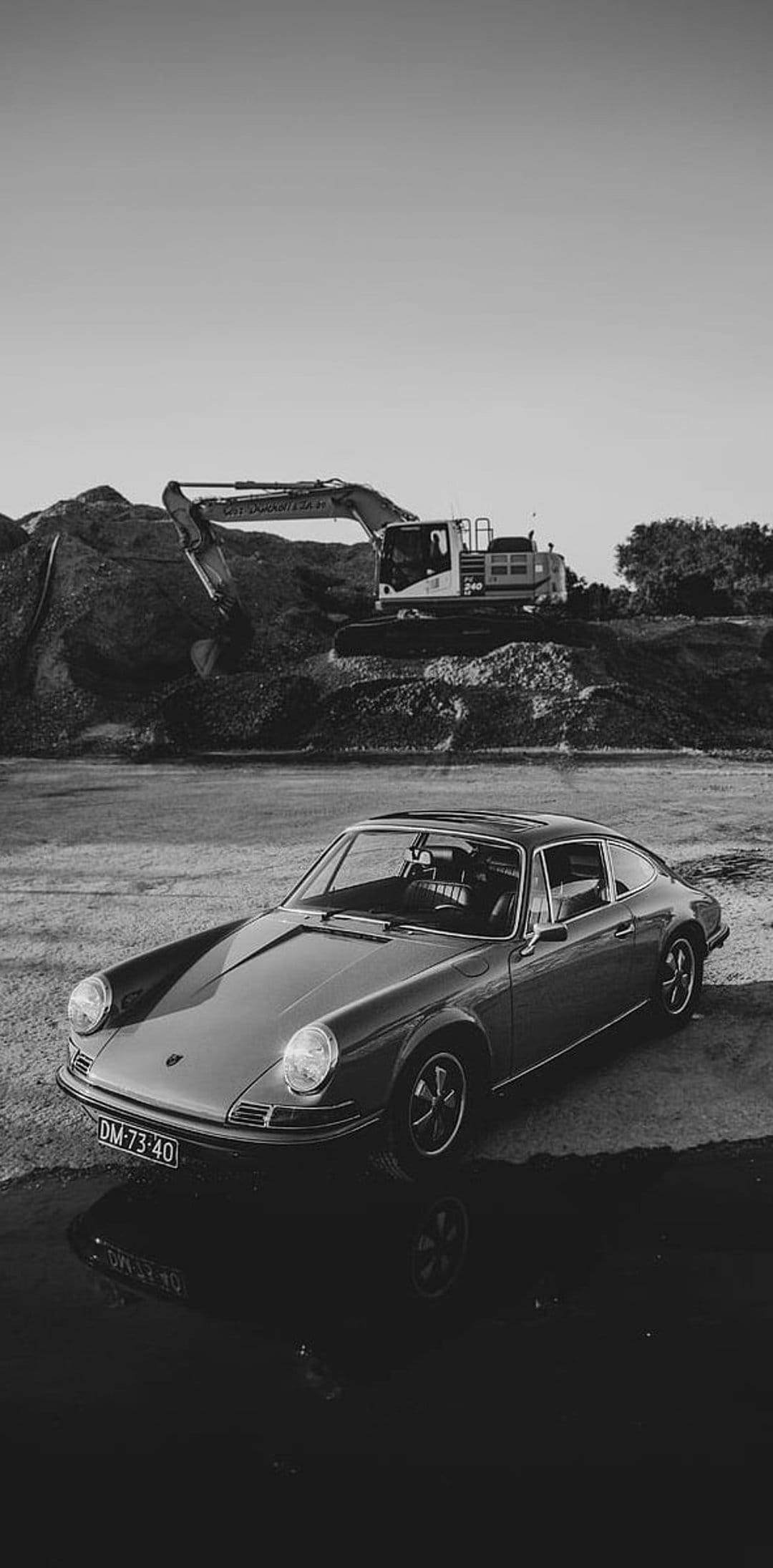Vintage Porsche 911 parked on dusty gravel with a heavy construction excavator in the blurred background.