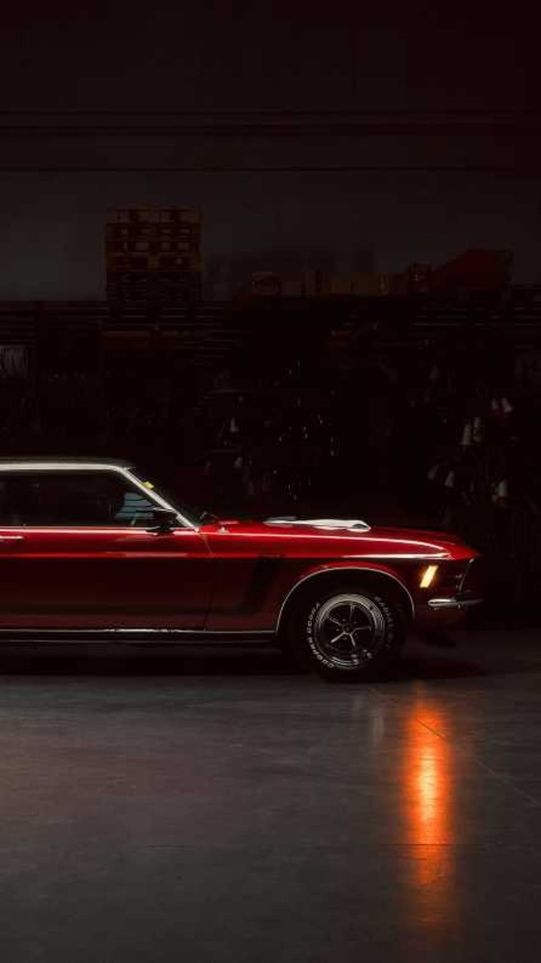 Red vintage Ford Mustang reflecting orange light in a dark garage, highlighting its iconic muscle car silhouette.