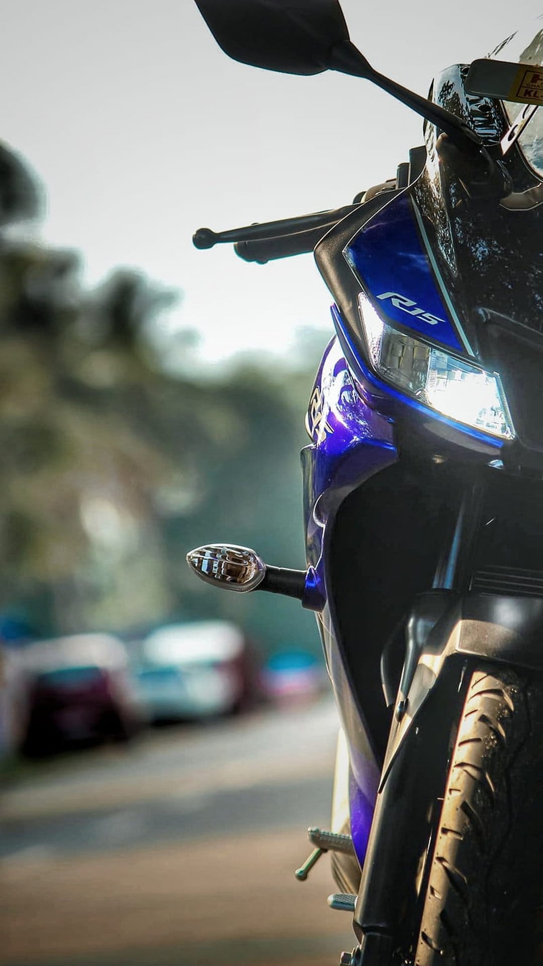 Blue Yamaha R15 motorcycle headlight with glowing LEDs and metallic fairing on a blurred road backdrop.