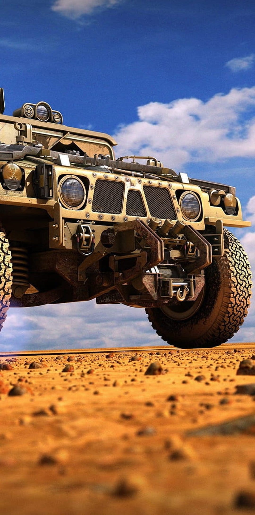 Tan military Humvee with heavy-duty tires drives over golden desert sand under a bright blue cloudy sky.