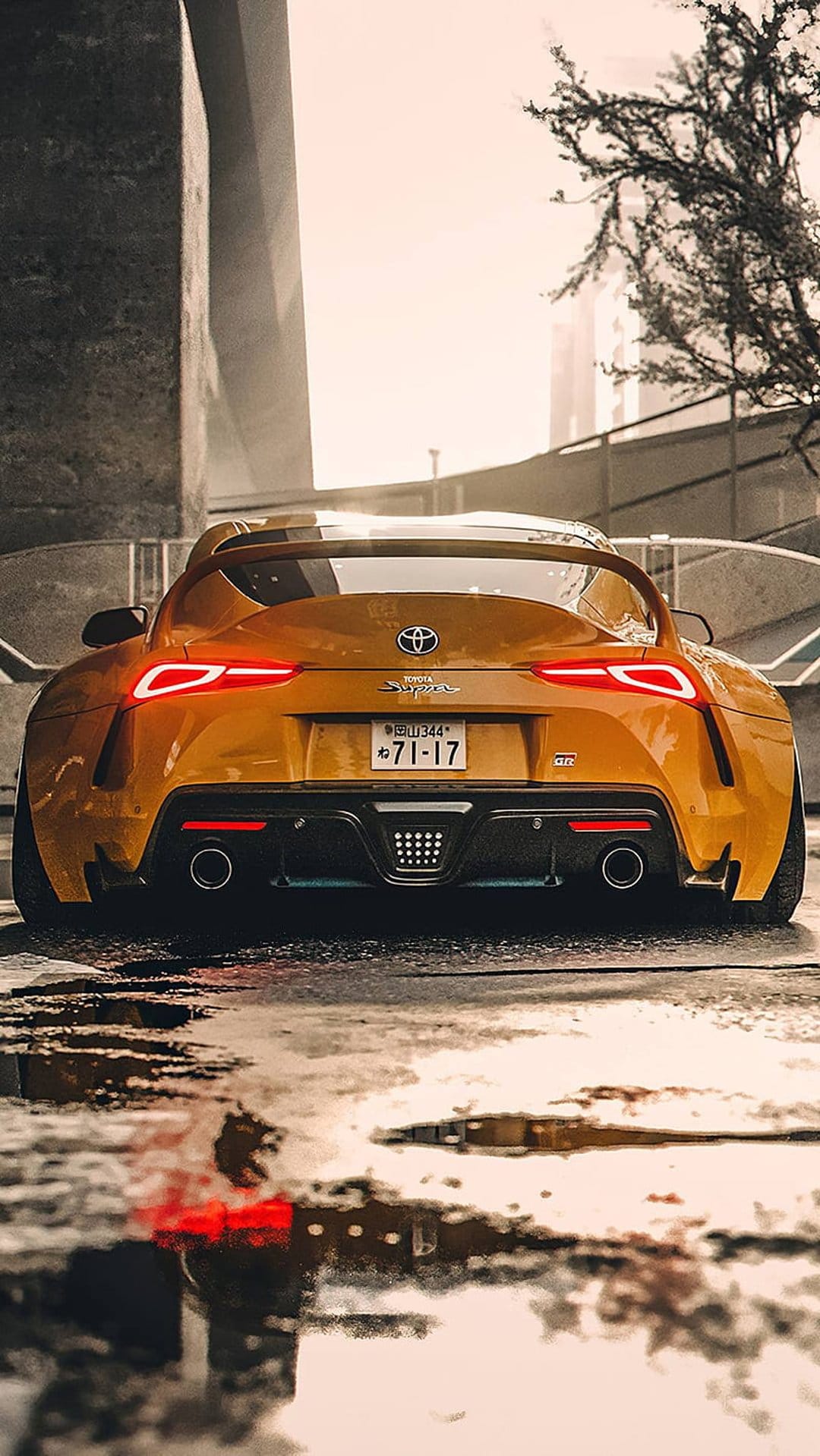 Toyota Supra GR rear view showcases glowing red taillights on a wet, reflective urban street at night.