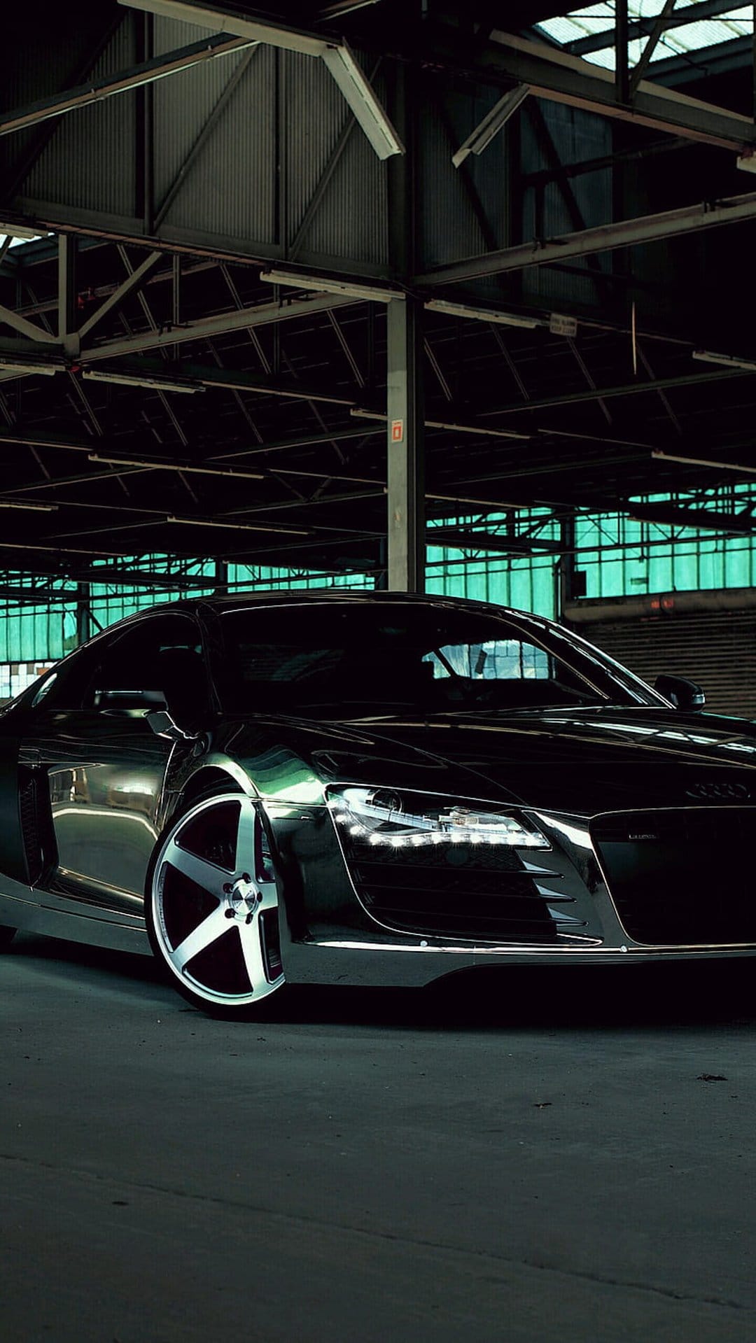 Black Audi R8 supercar with glowing LED headlights parked in a dark warehouse with green tinted windows.