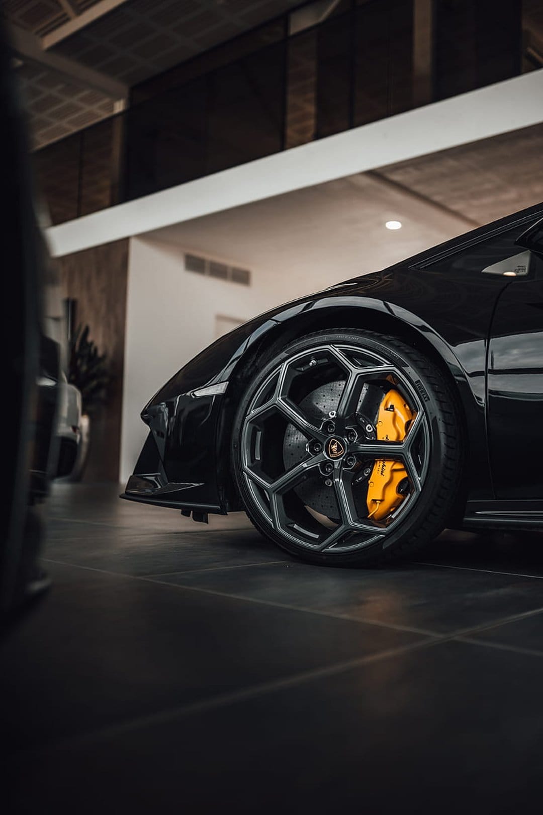 Lamborghini multi-spoke wheel and yellow brake calipers reflected on a glossy floor in a luxury showroom.