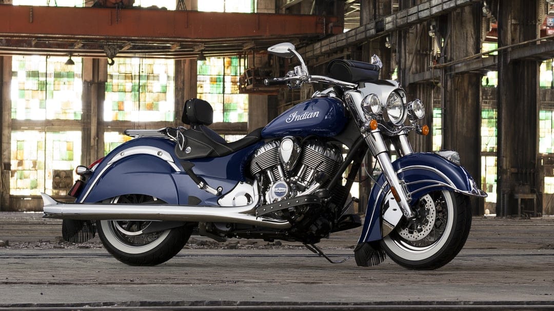 Blue Indian Chief Vintage motorcycle with chrome accents and whitewall tires in a weathered industrial warehouse.