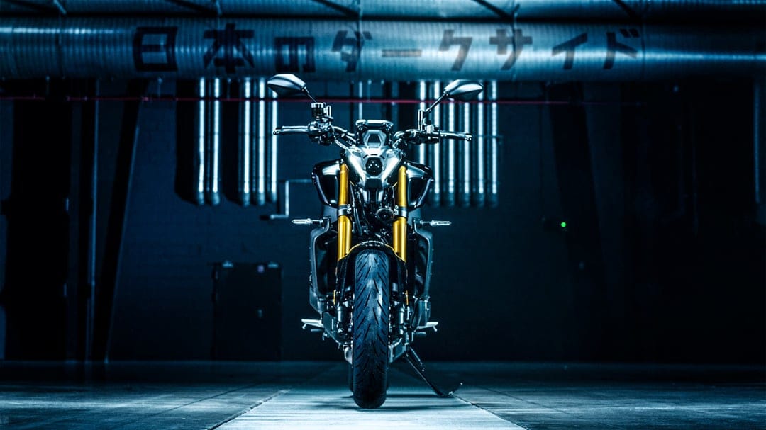 Dark Yamaha MT-09 SP motorcycle with gold forks centered in a blue industrial garage with Japanese text.