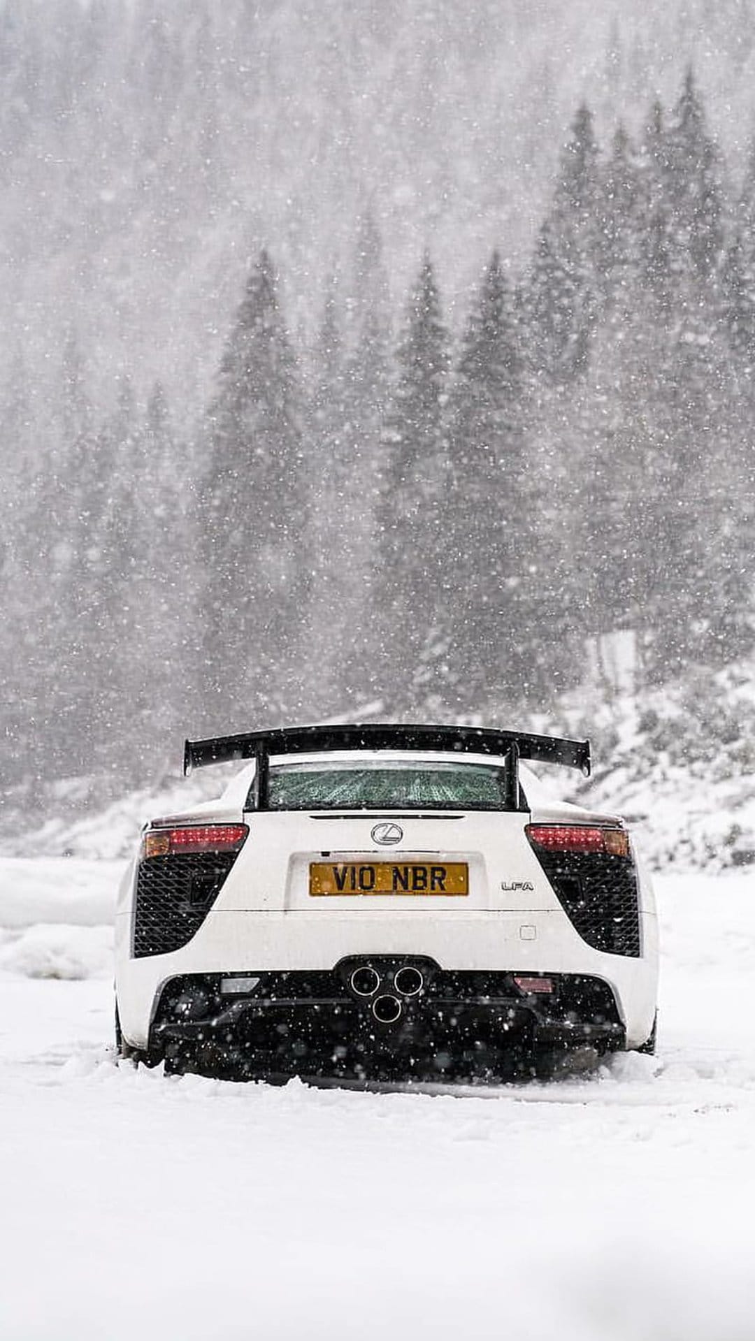 Lexus LFA rear view with triple exhaust pipes and a large spoiler parked in a snowy evergreen forest at dusk.
