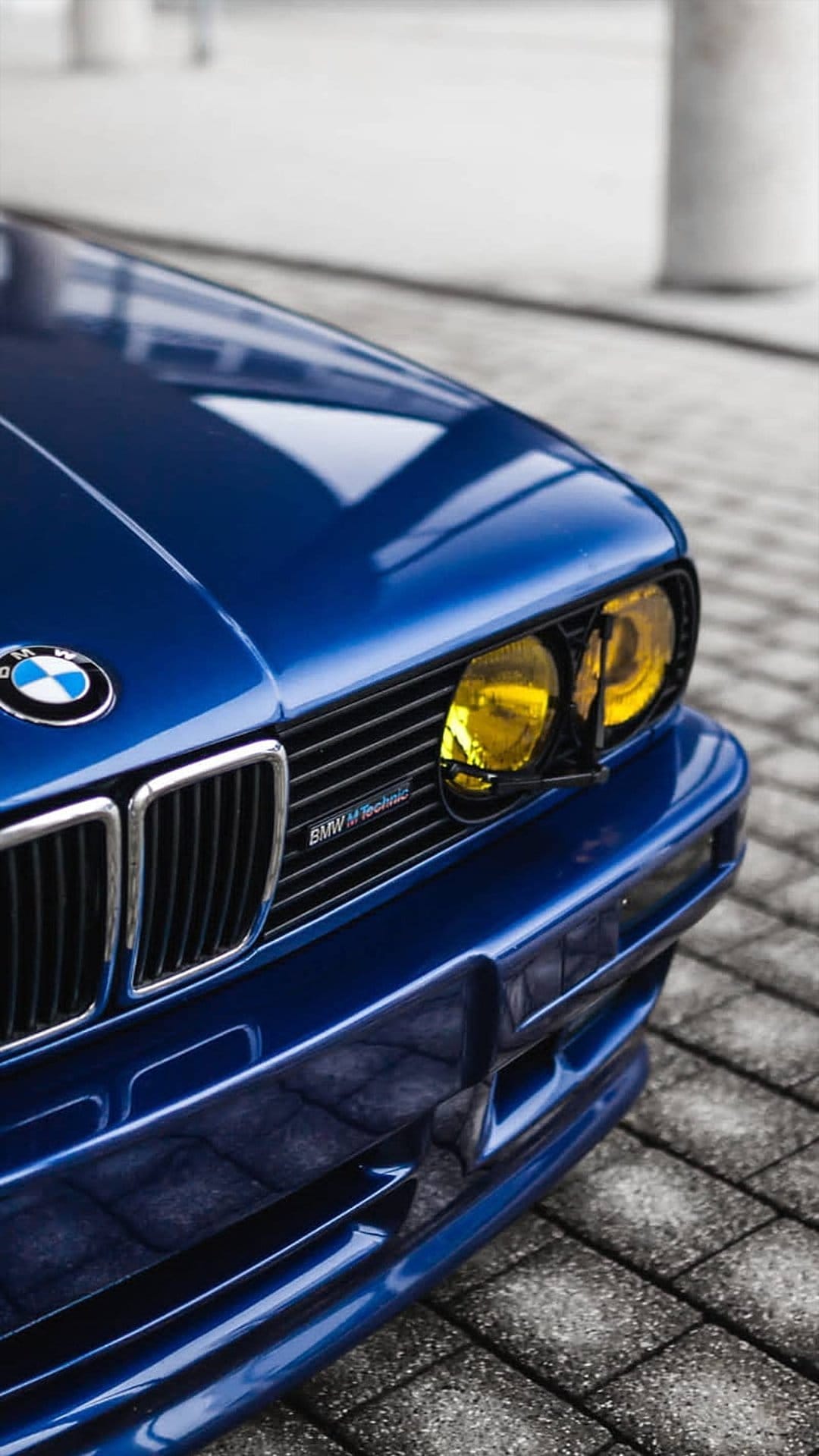 Blue BMW M Technic front end features bright yellow headlights and a polished kidney grille in a close-up shot.