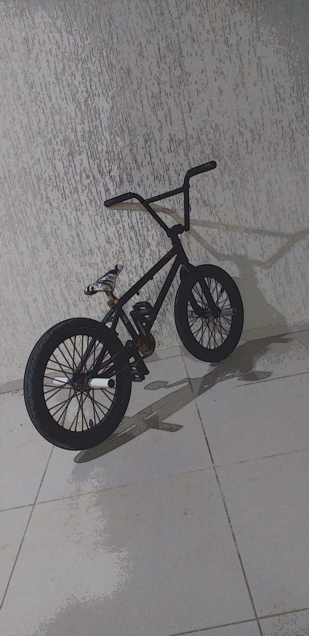 Black BMX bicycle rests against a textured stone wall with sharp shadows stretching across the tiled ground.