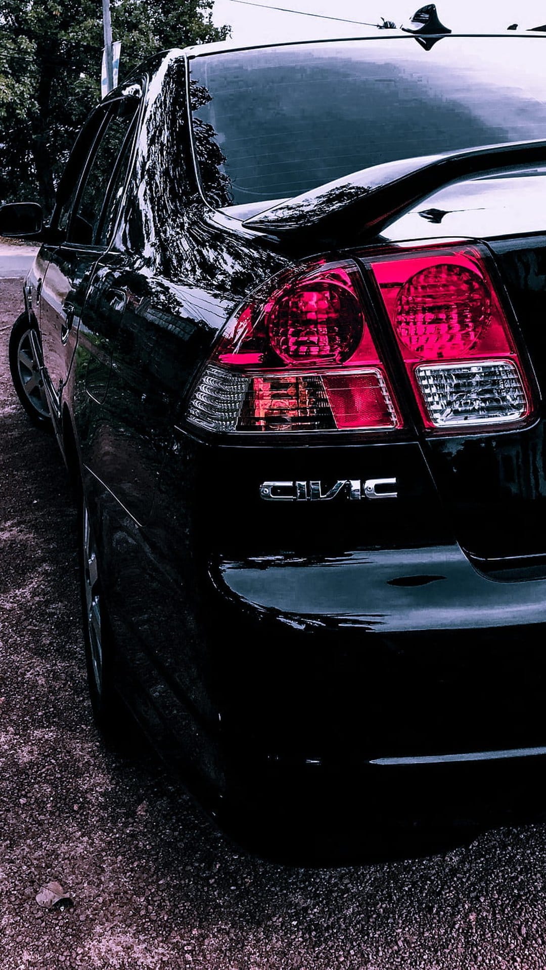 Black Honda Civic rear exterior showing glowing red taillights and chrome lettering on a gravel ground.