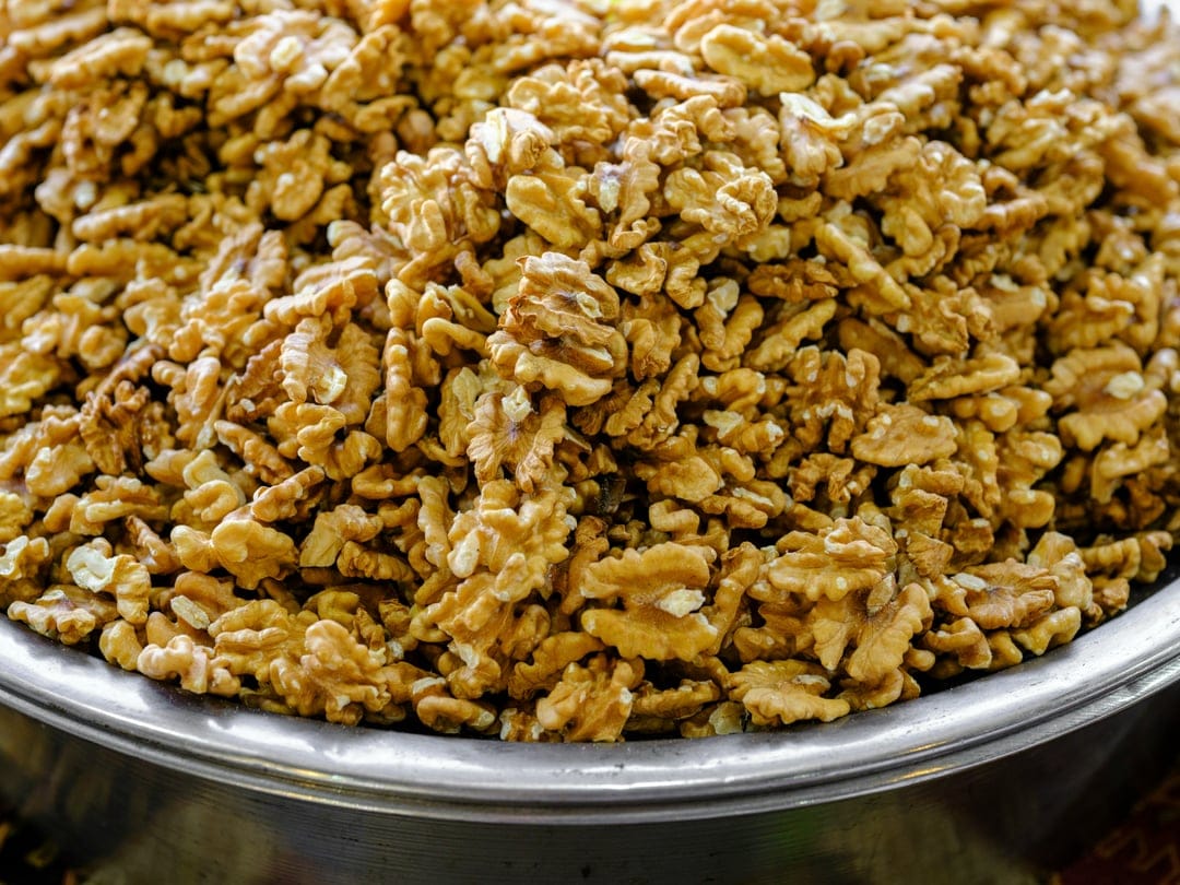 Shelled walnuts with deep ridges and grooves pile together in a top-down view showing warm brown textures.