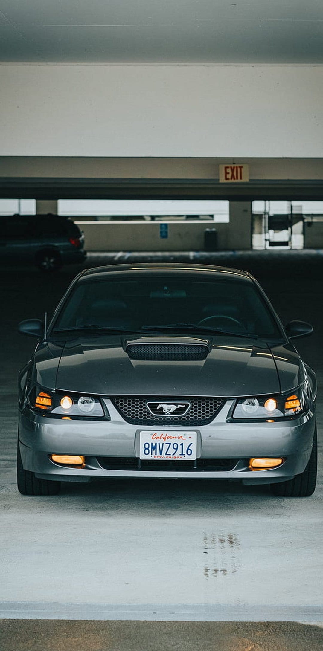 Ford Mustang front grille with glowing headlights and amber fog lamps inside a dark concrete parking garage.
