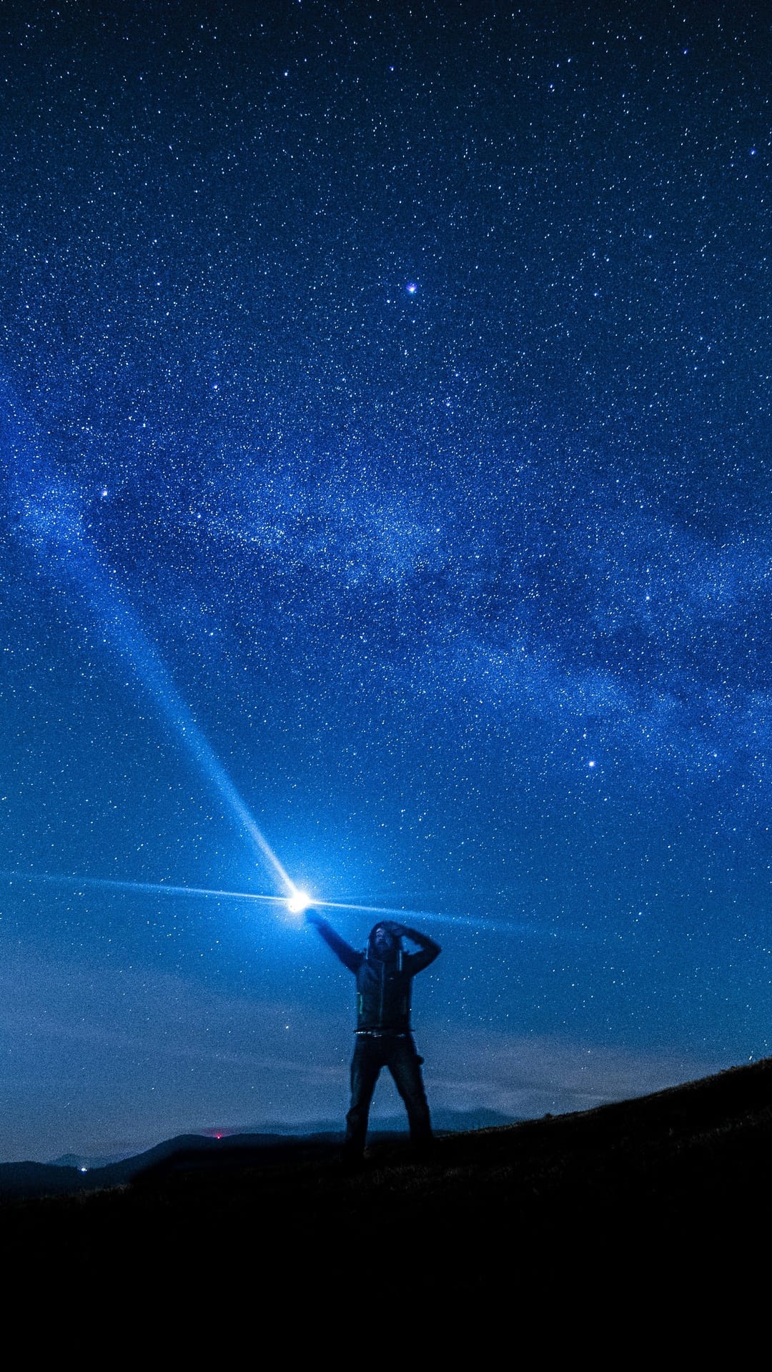 Lone person standing under a glowing Milky Way arch framed by dark rock formations in a starry night sky.