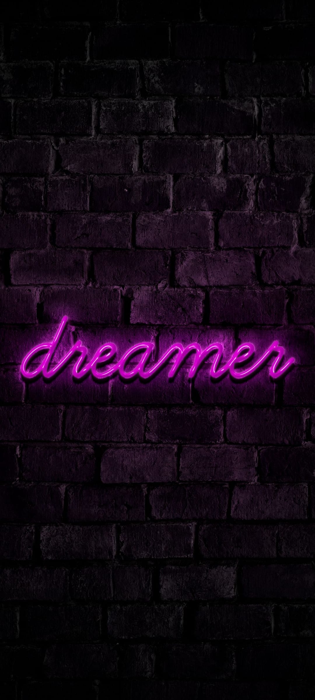 Purple neon sign spelling Dreamer mounted on a dark textured brick wall with a soft violet ambient glow.