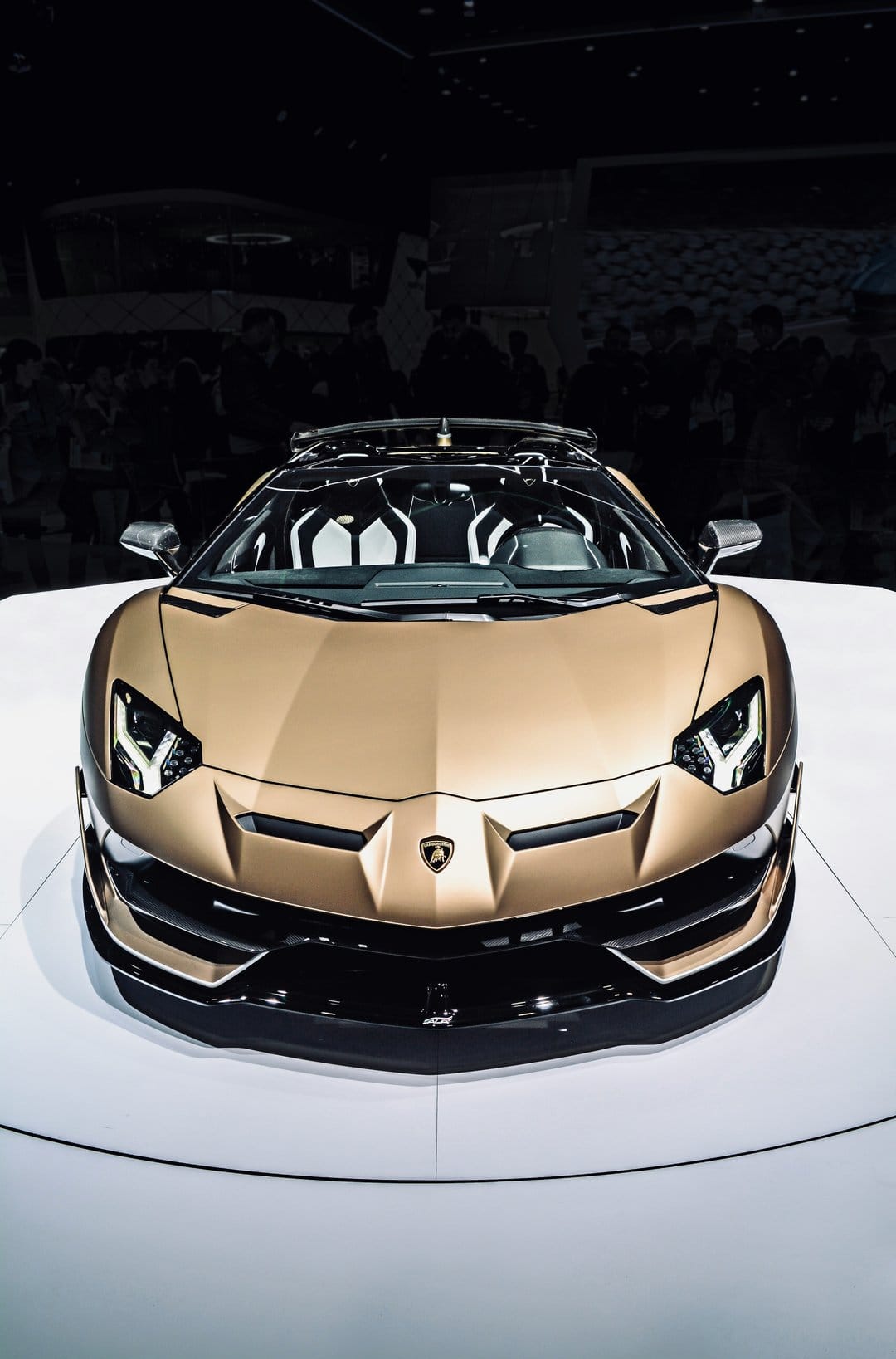 Golden brown Lamborghini Aventador SVJ Roadster front view with sharp headlights and an open convertible top.