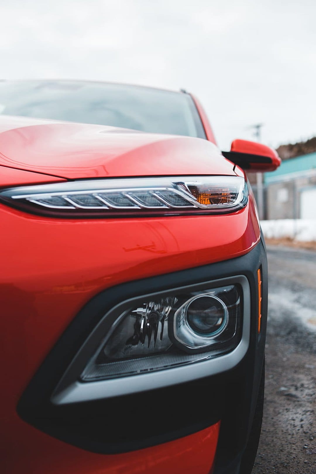 Hyundai Kona headlight and slim LED daytime running light glow against vibrant red paint with a blurred background.