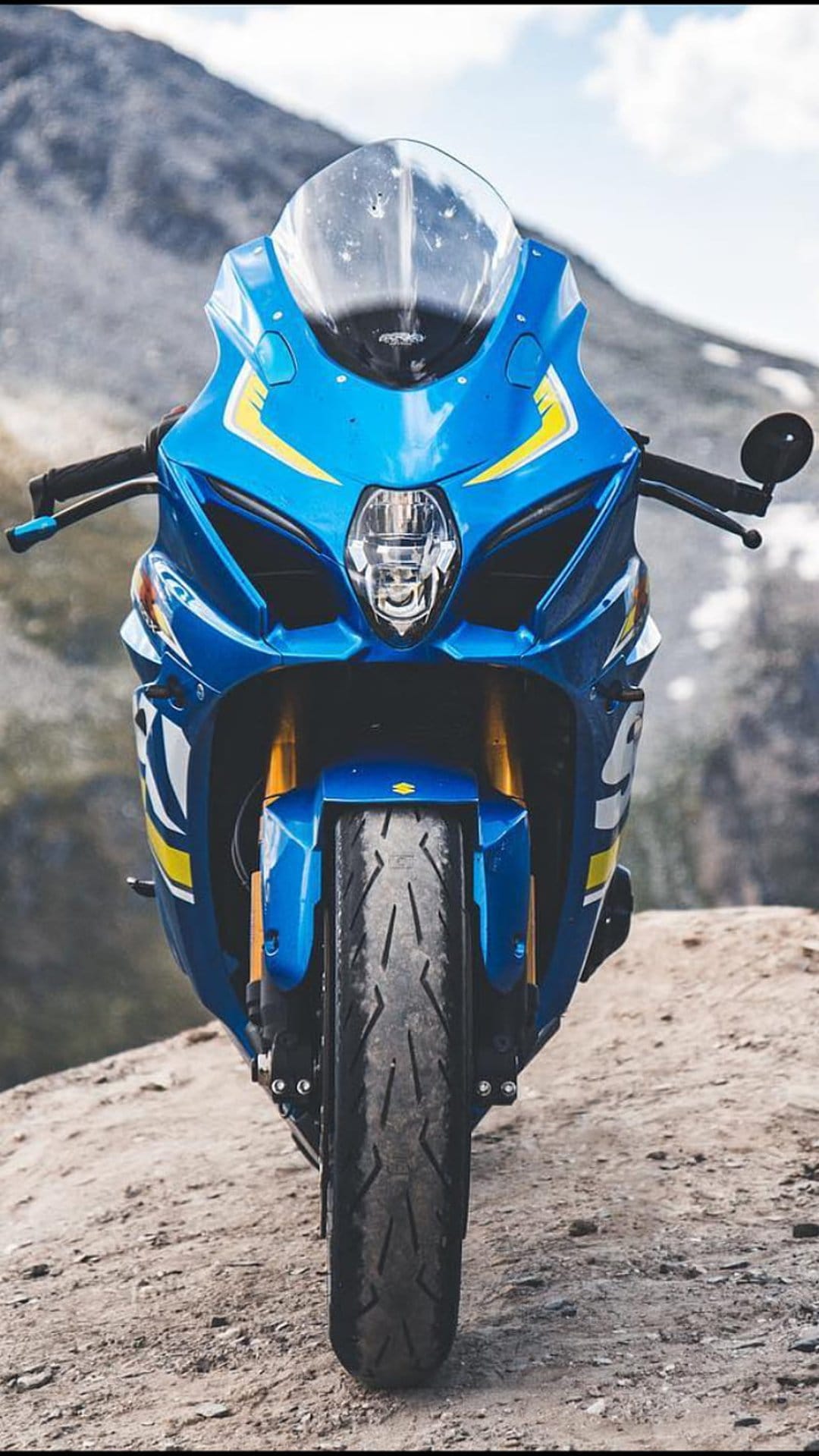 Suzuki GSX-R sportbike with blue fairings and yellow accents parked on a rocky, mountainous terrain.