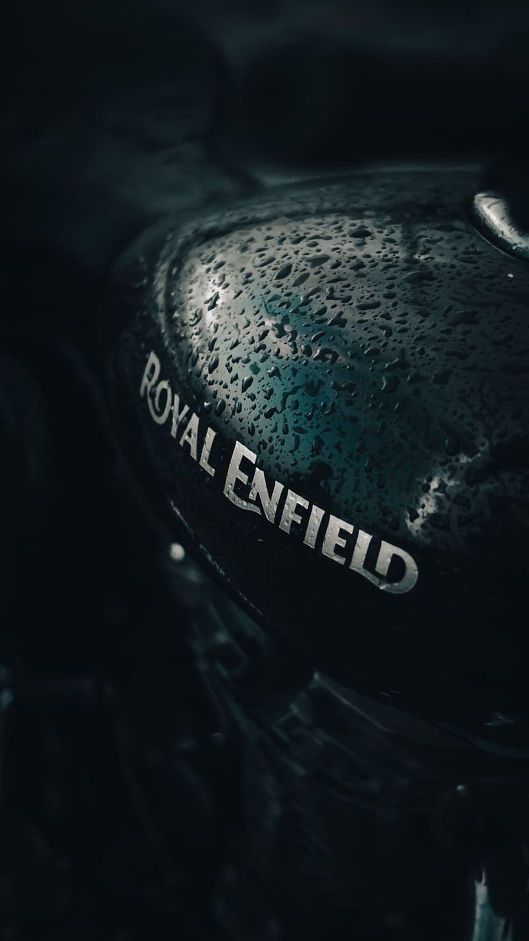Royal Enfield fuel tank with glistening raindrops and chrome logo in a moody close-up automotive photograph.